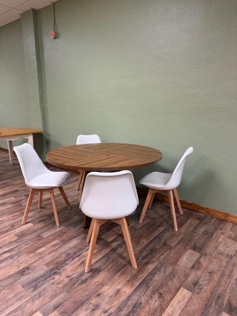 A round wooden table surrounded by four white chairs in a room with green walls and wooden flooring.