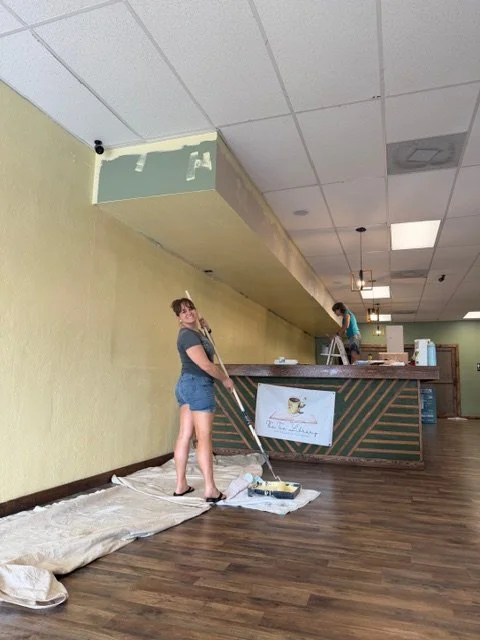 People painting the ceiling in a room with a checkout counter in the background.