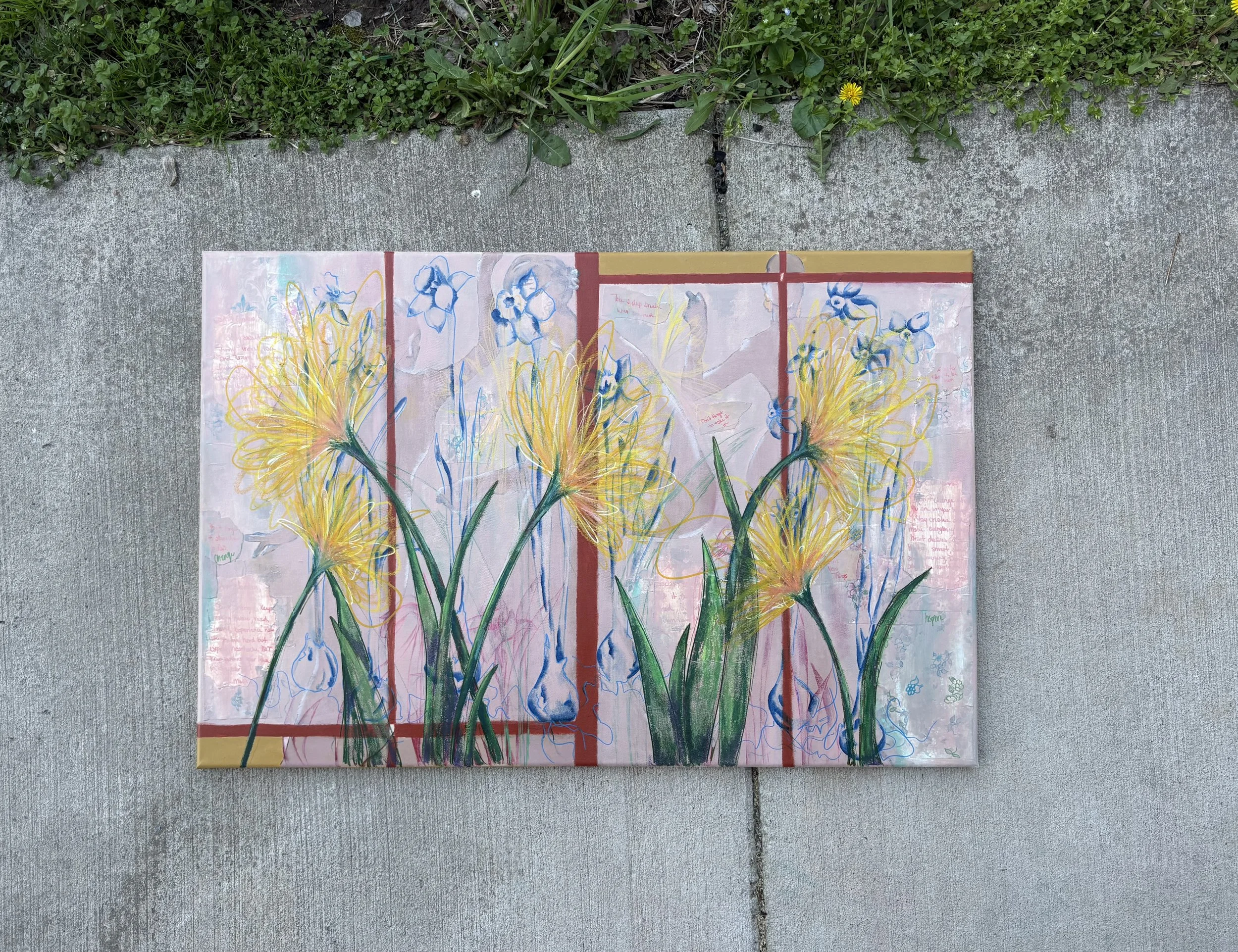 Abstract floral artwork with yellow, green, and blue colors on paper, placed on a concrete surface next to grass and small yellow flowers.