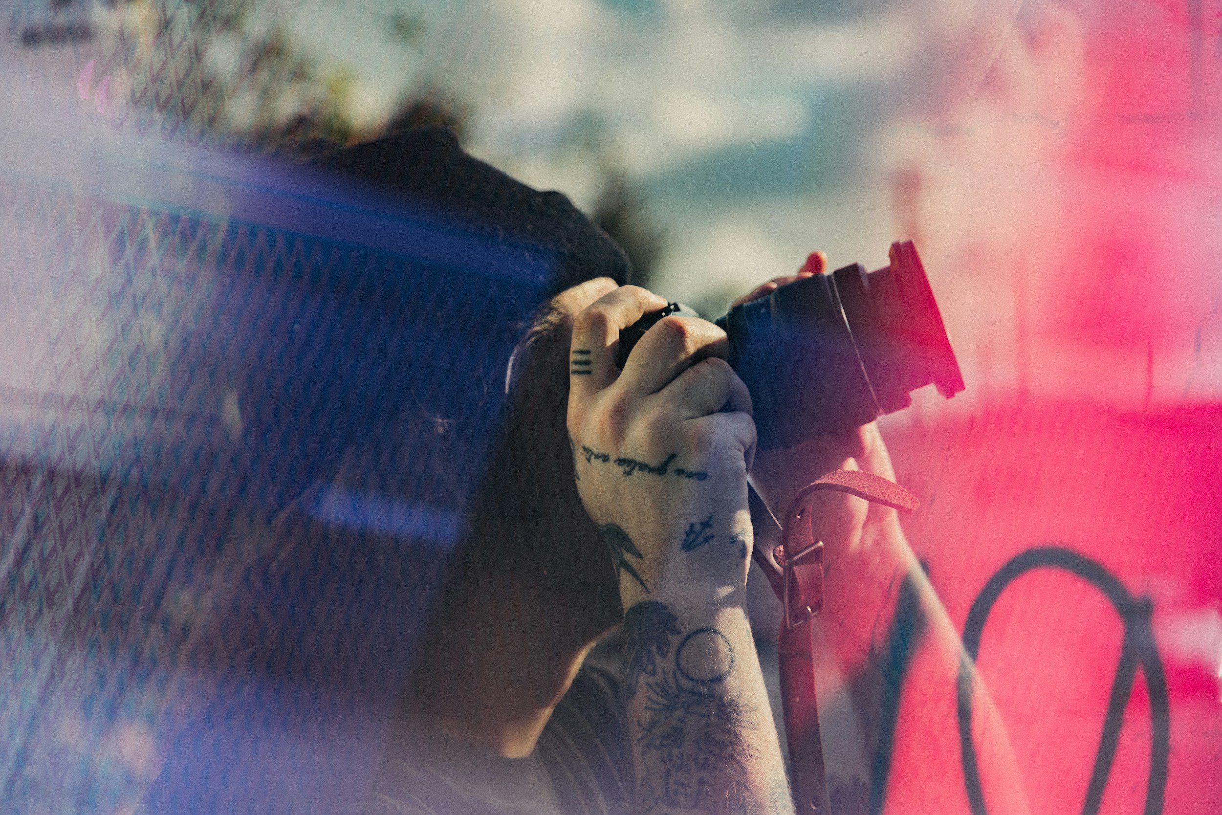 Persona con tatuajes sosteniendo una cámara, con efecto de luz y reflejos.