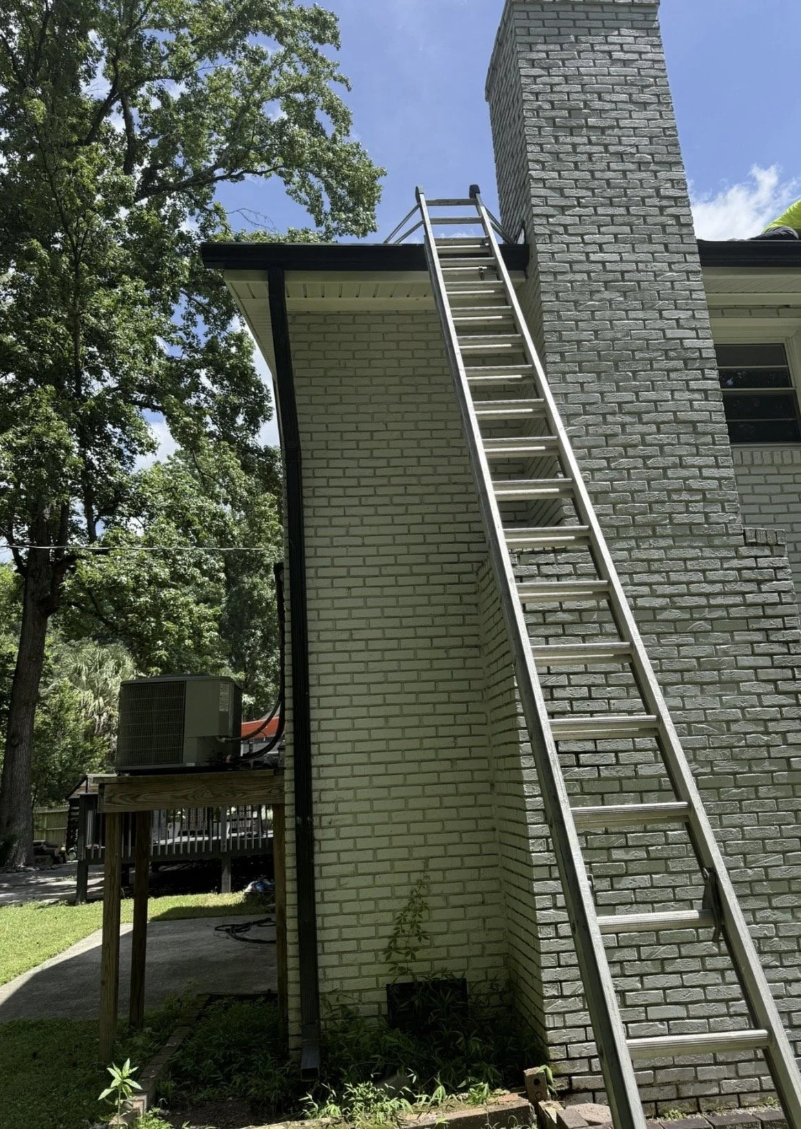 Black residential rain gutters and downspout installed along the roofline of a white brick home.