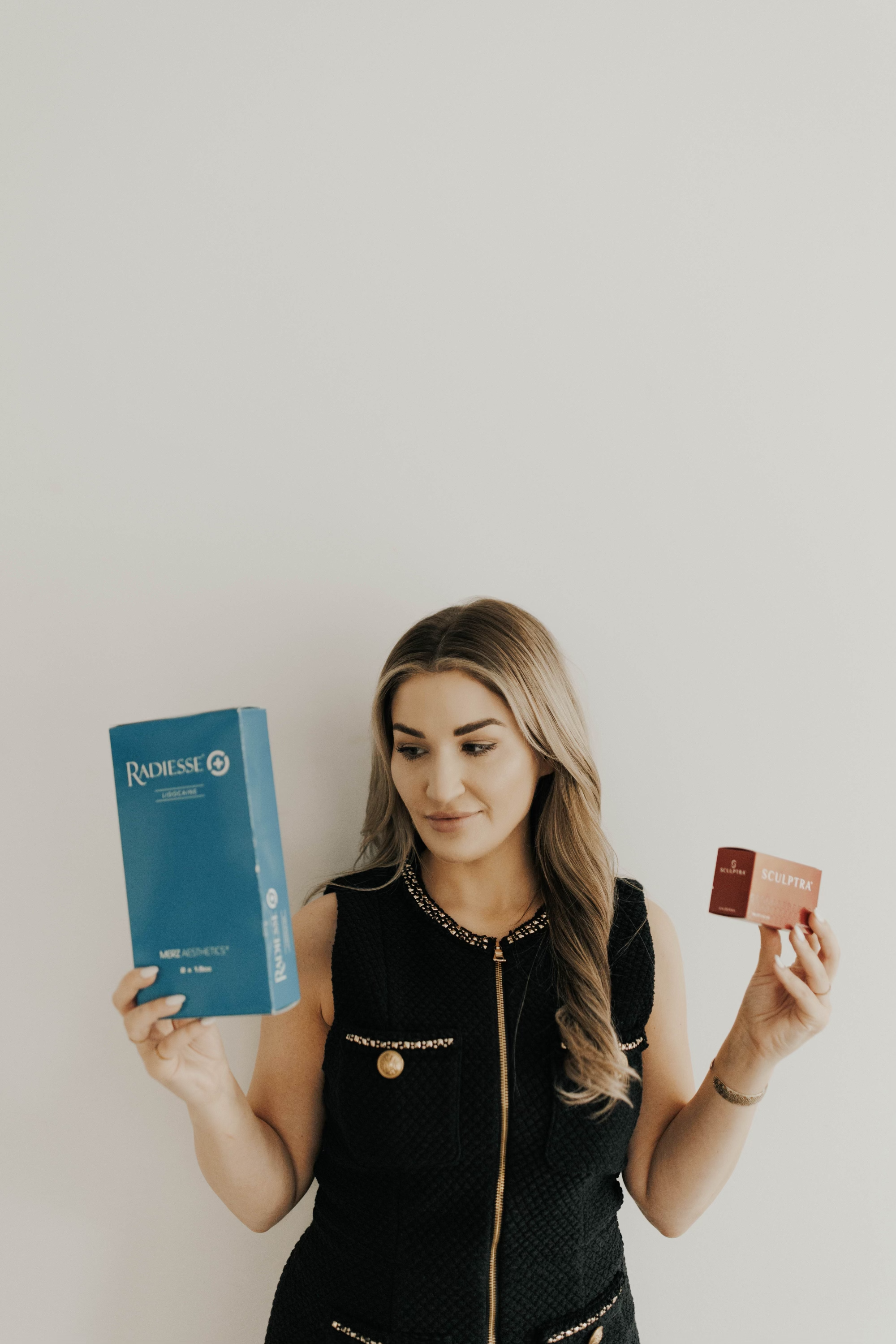 Chrissy Poharatnyj FNP-BC, founder of Golden Aesthetics, holding Radiesse and Sculptra biostimulator filler boxes