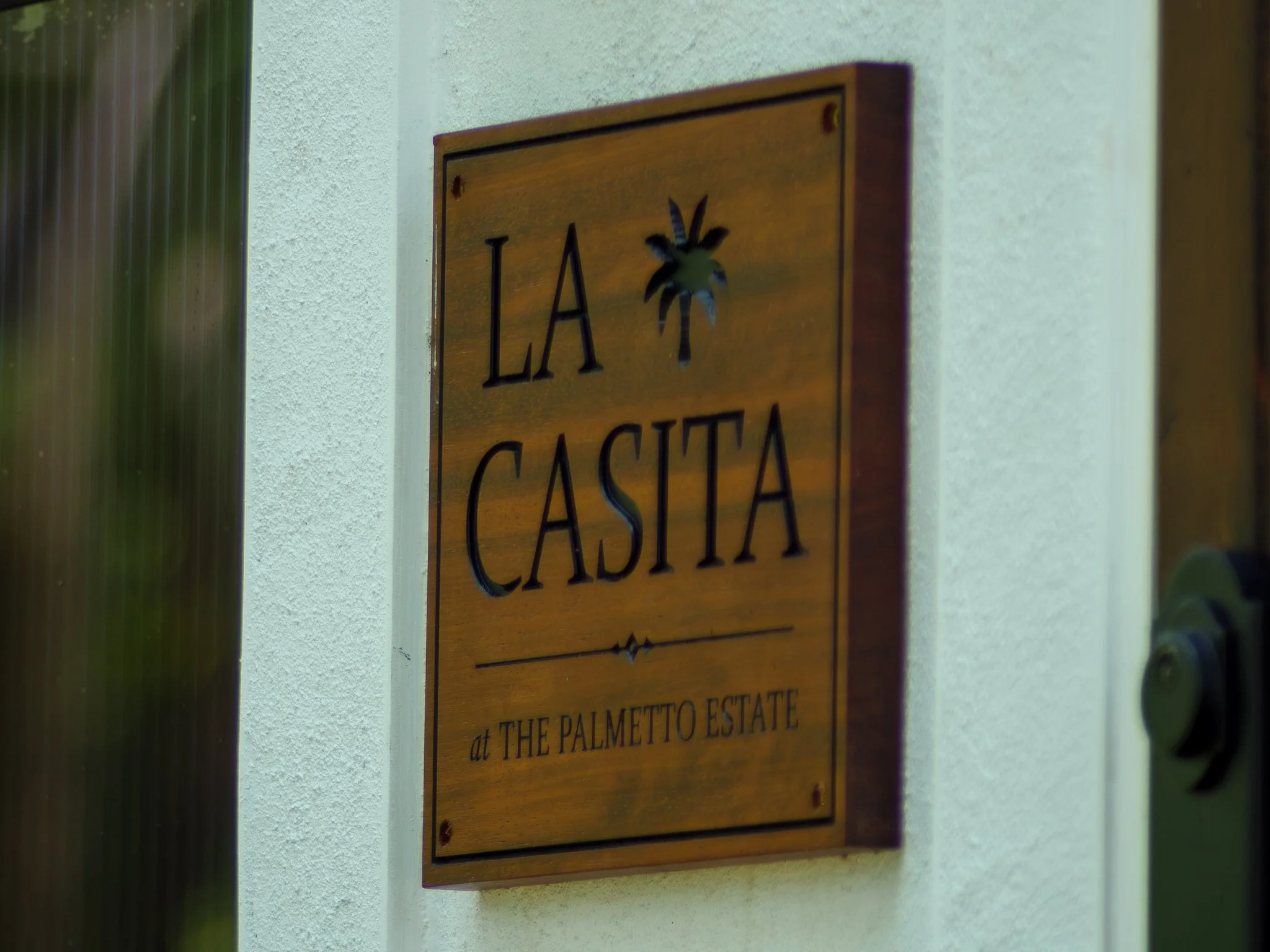 A wooden sign on a white wall that reads 'LA CASITA' with a small decorative image of a palm tree above the text.