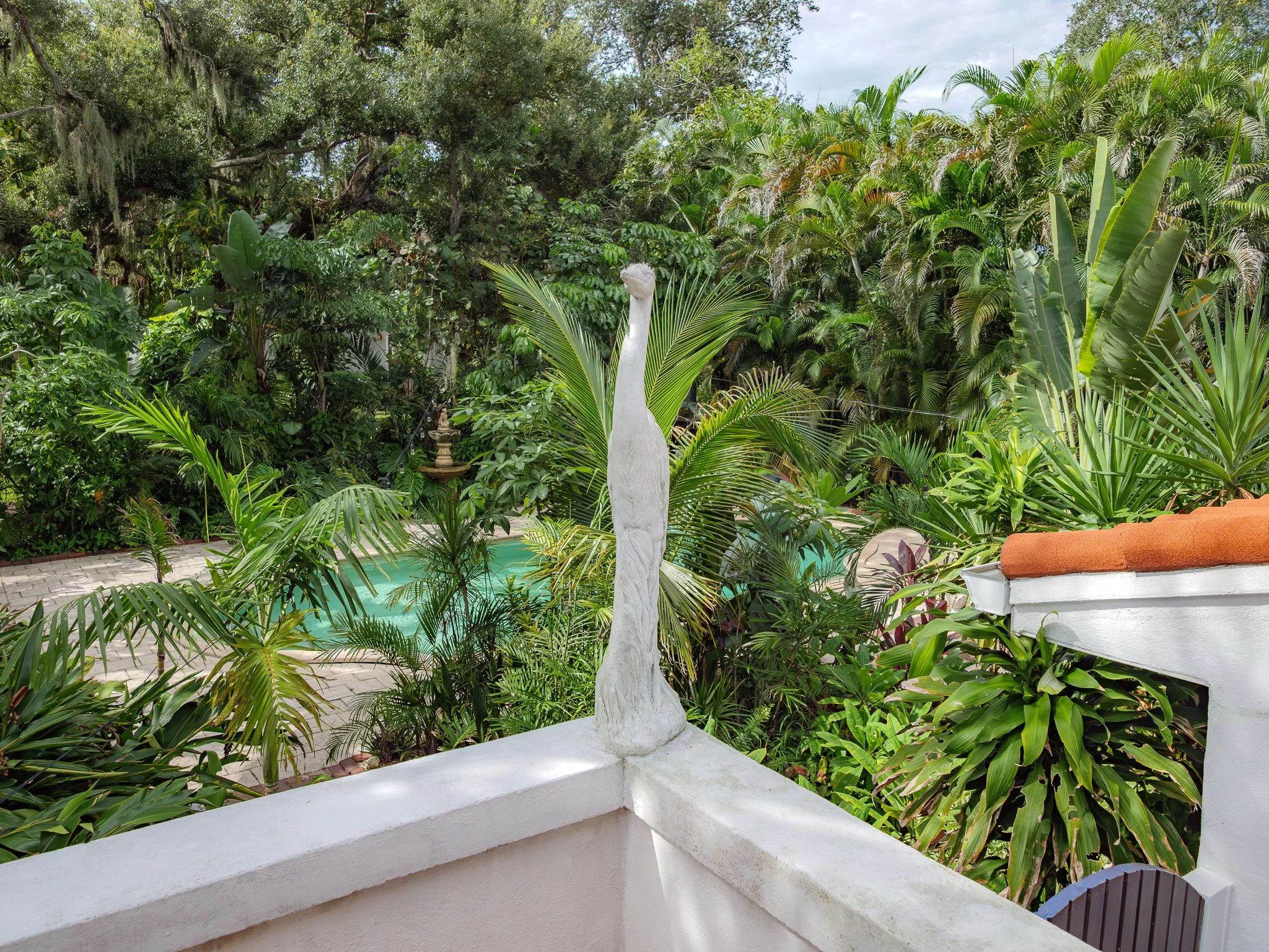White statue of a heron on a patio with lush green tropical plants in the background.