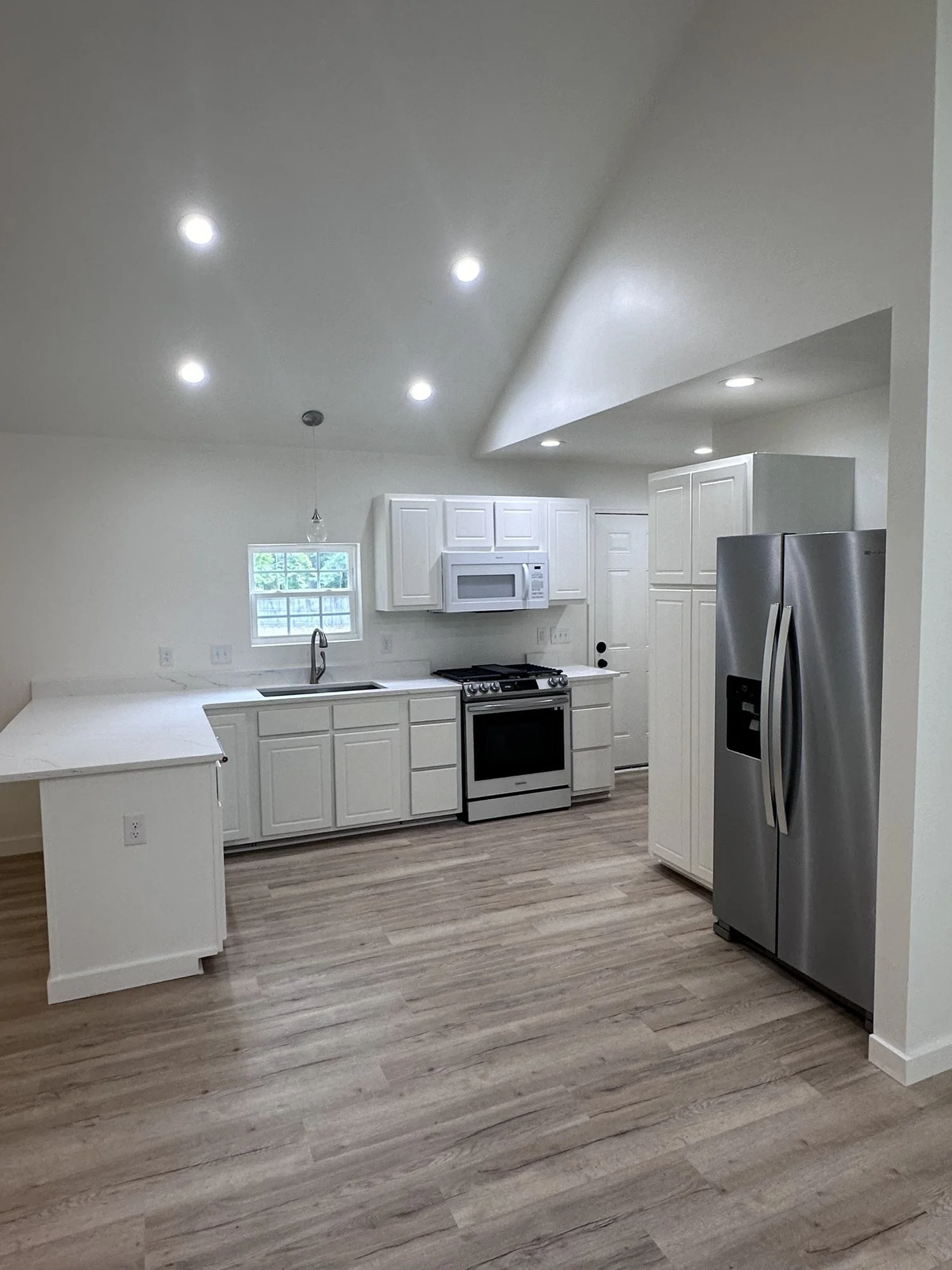 Kitchen remodel: white cabinetry, new appliances and flooring under a vaulted ceiling.