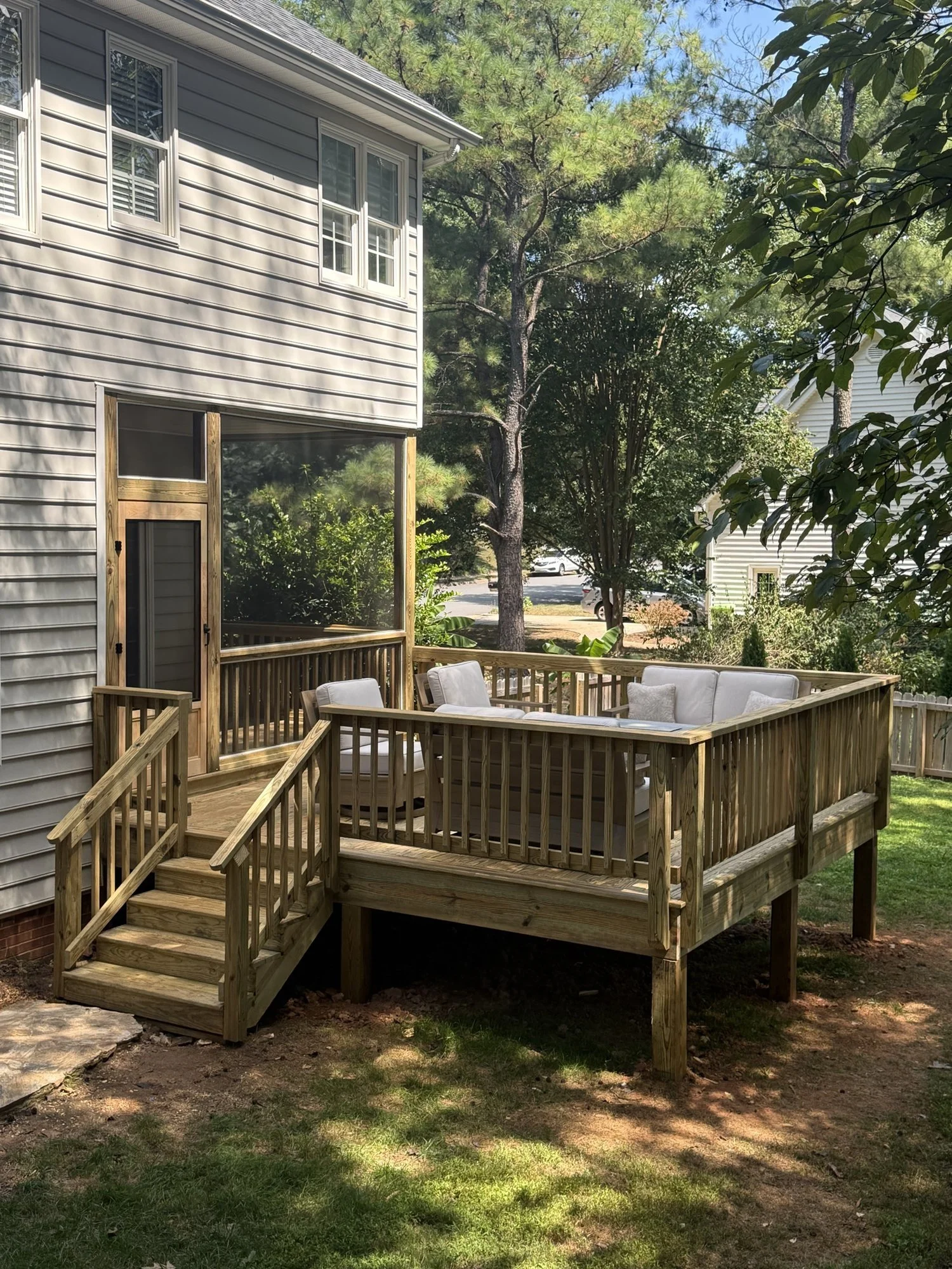 New pressure-treated deck with steps and railing, built off a screened porch.