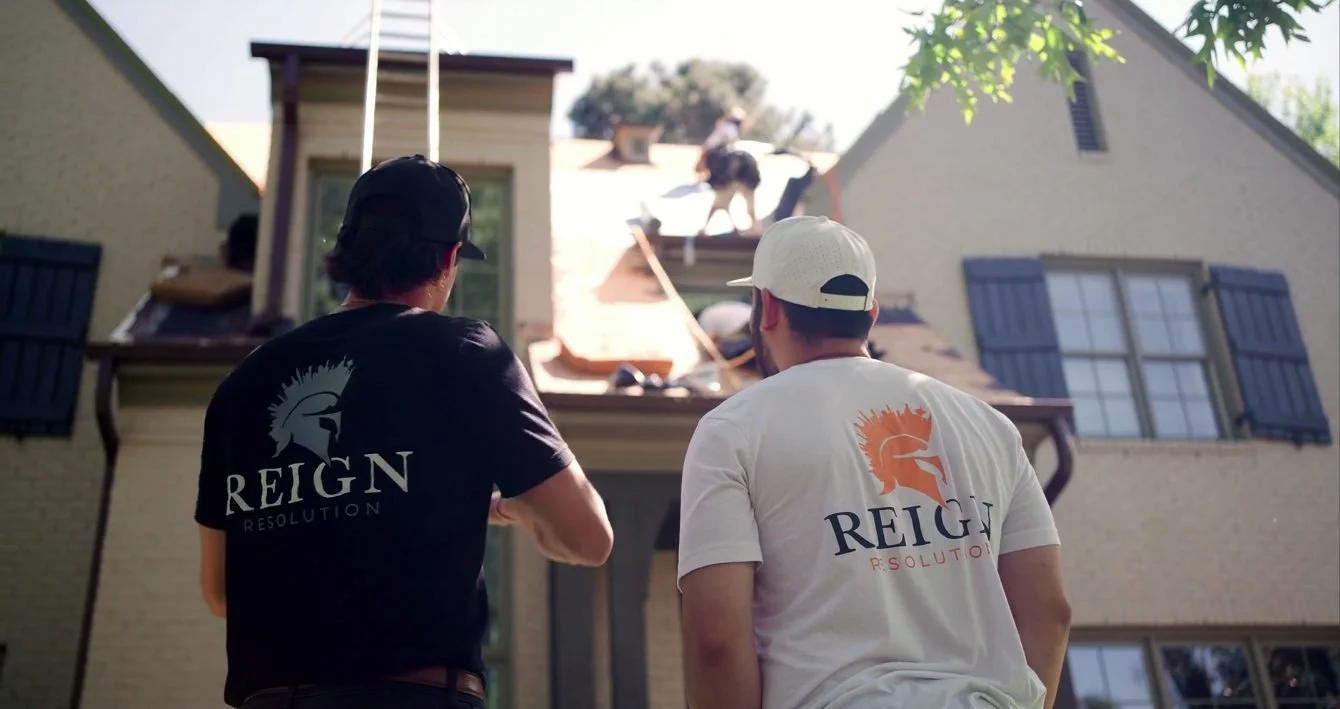 Two Reign Resolution crew members in branded shirts looking up at a roof during a repair