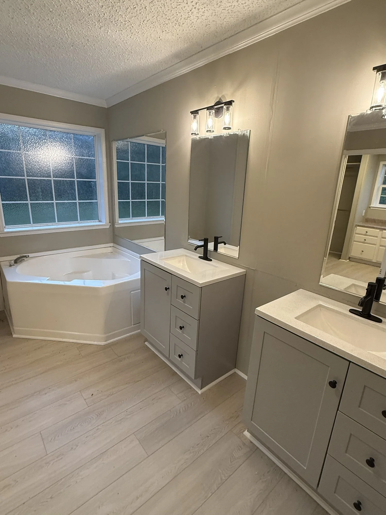Bathroom remodel: two vanities with new tops and fixtures, corner tub and plank flooring.