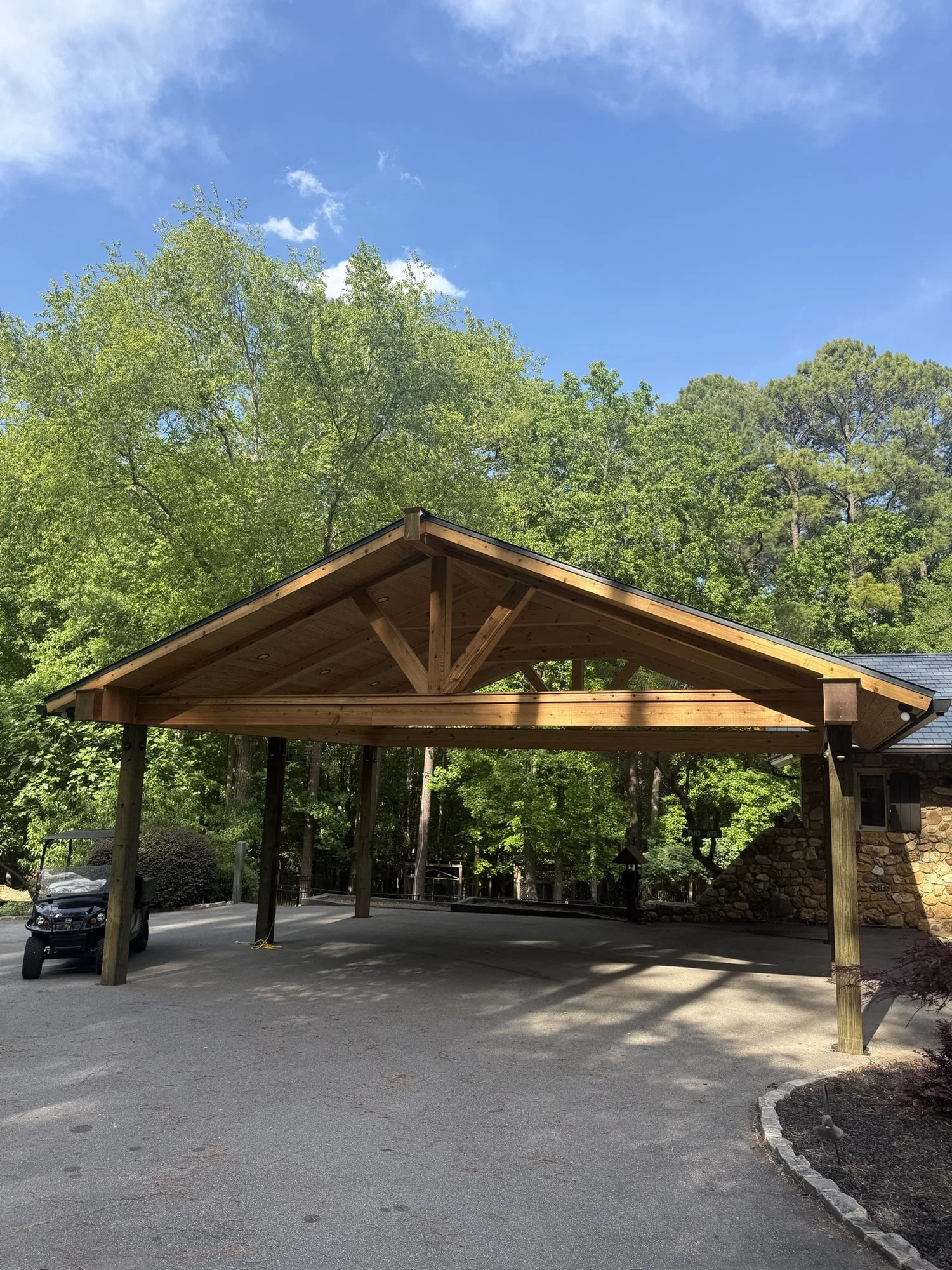 Timber-frame pavilion: an open-air structure with exposed beams over a parking and gathering area.