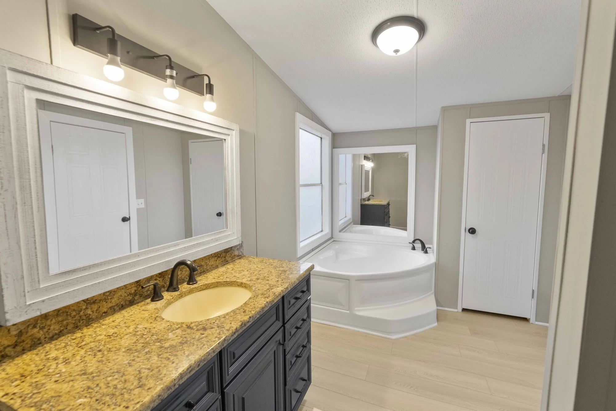 Bathroom remodel by Reign Resolution: new vanity with granite top, framed mirror, lighting and a corner soaking tub