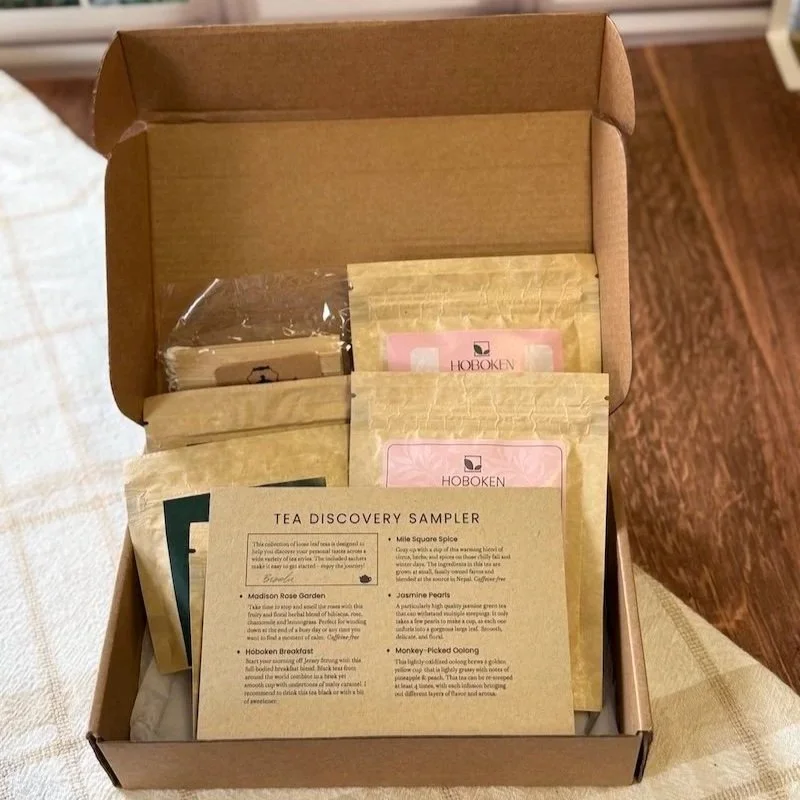 an open loose leaf tea sampler box filled with packets of tea and a notecard