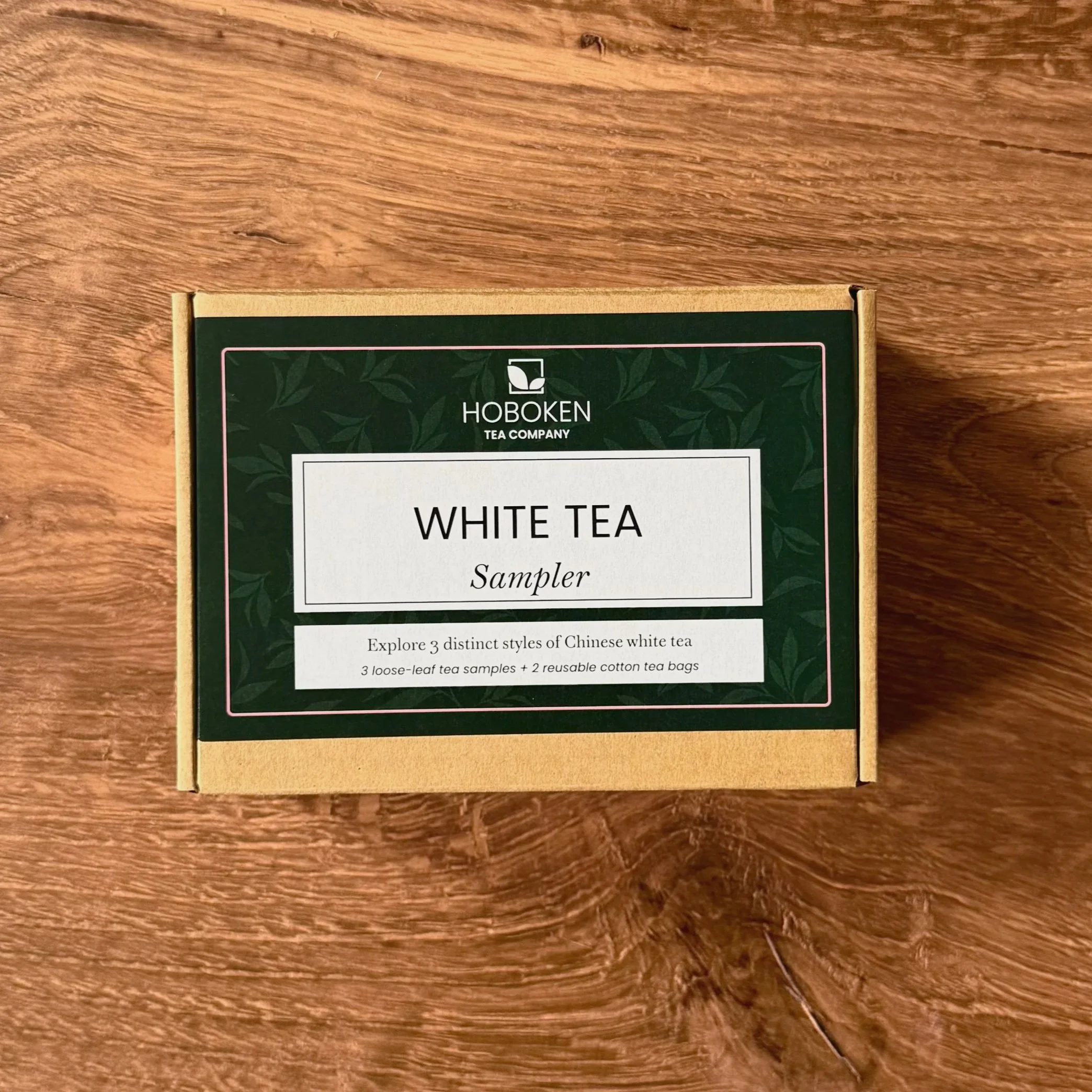 a box with a green Hoboken Tea Company label reading "White Tea Sampler" on a wood surface