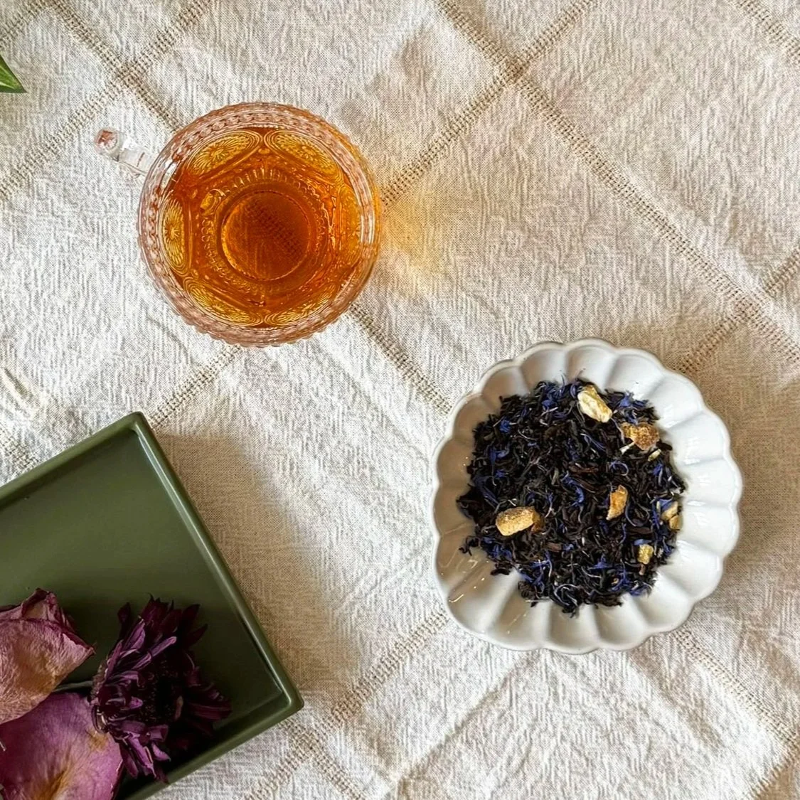 a cup of Liberty Grey black tea next to a dish of dry tea leaves and some dry roses