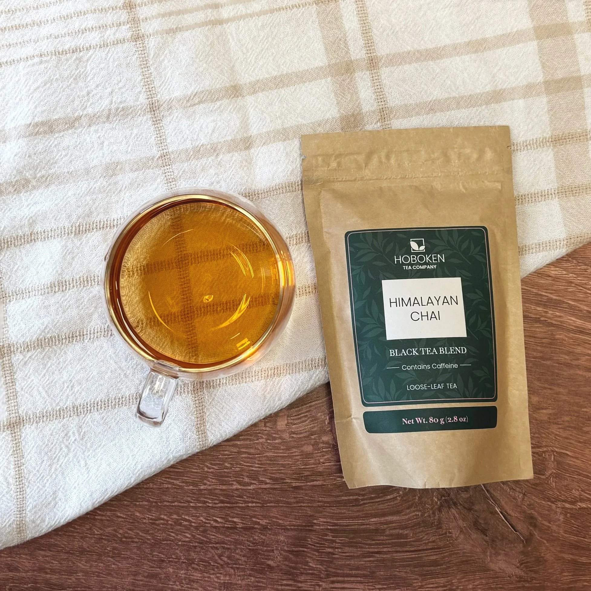 a package of loose leaf Himalayan Chai black tea from Hoboken Tea Company next to a glass of black tea on a wood surface