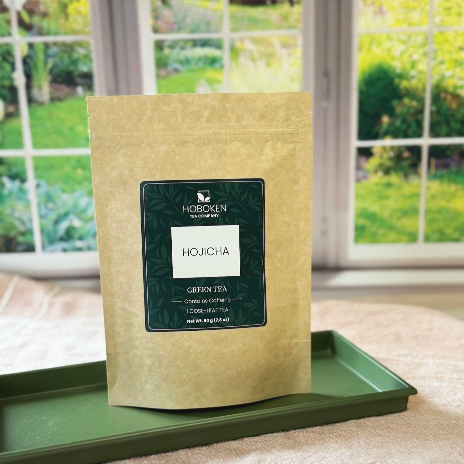 a packet of Hojicha roasted green tea on a tray in front of a window with a spring garden in the background