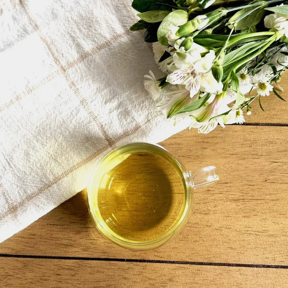a cup of green tea on a wood table next to a bunch of white flowers