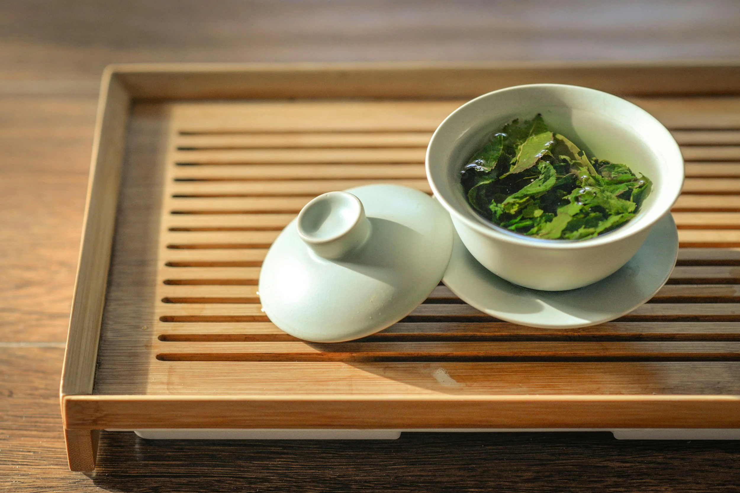 Steeped green tea leaves in a porcelain gaiwan on a bamboo tray