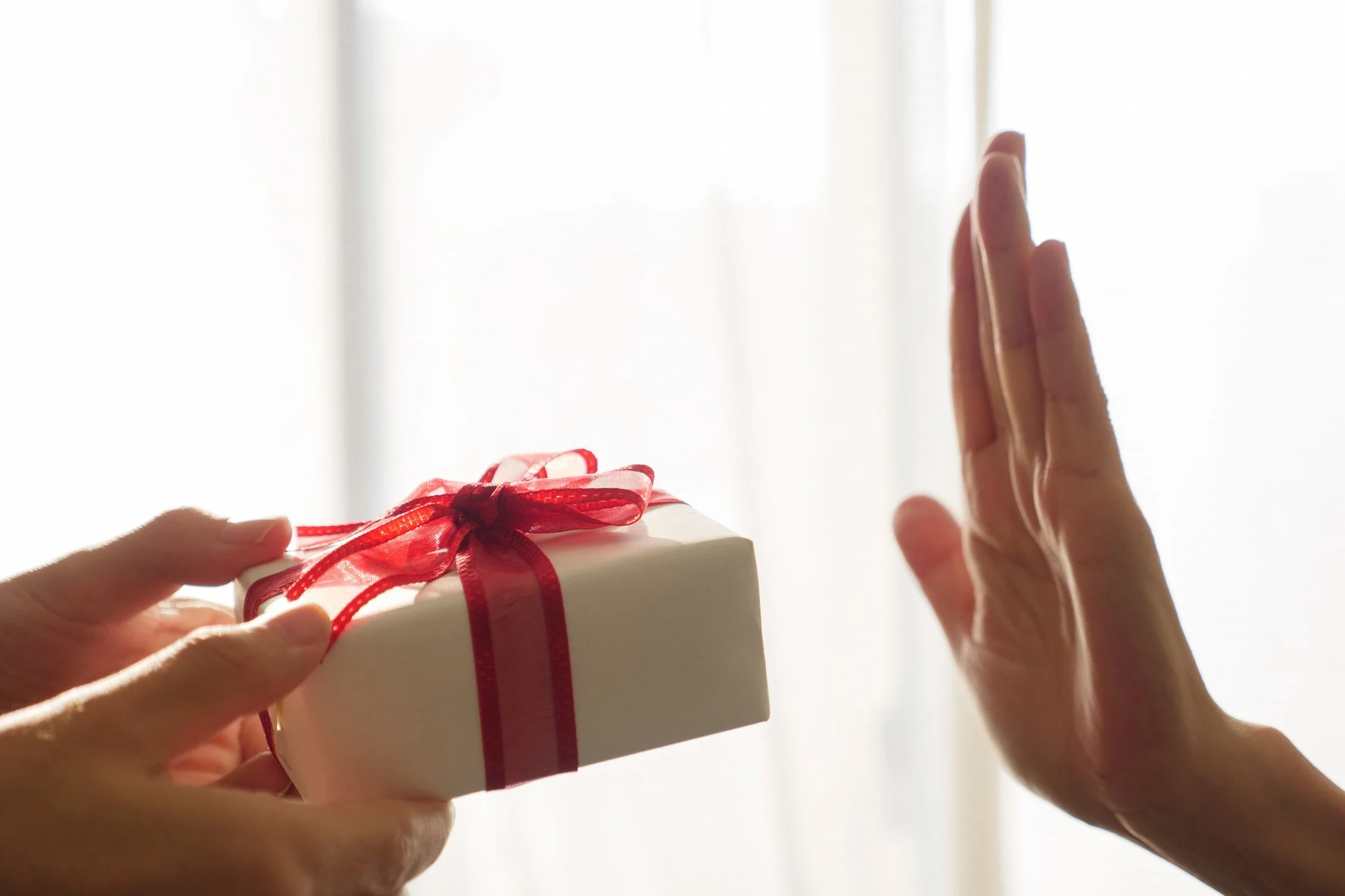 A person's hand gesturing to reject a wrapped gift presented by another person