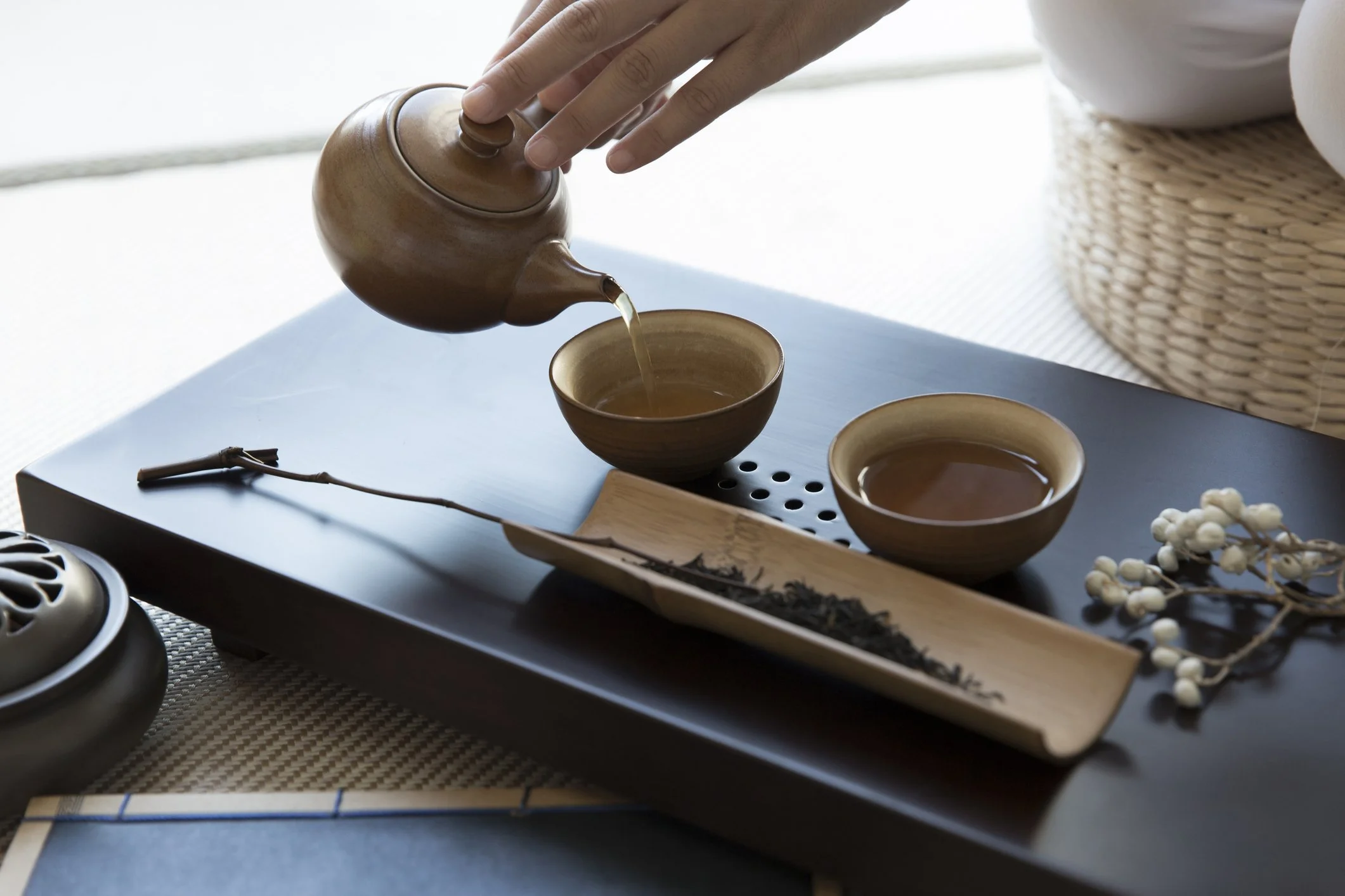 hands pouring tea from  small clay teapot into cups on a traditional Gong Fu tea tray