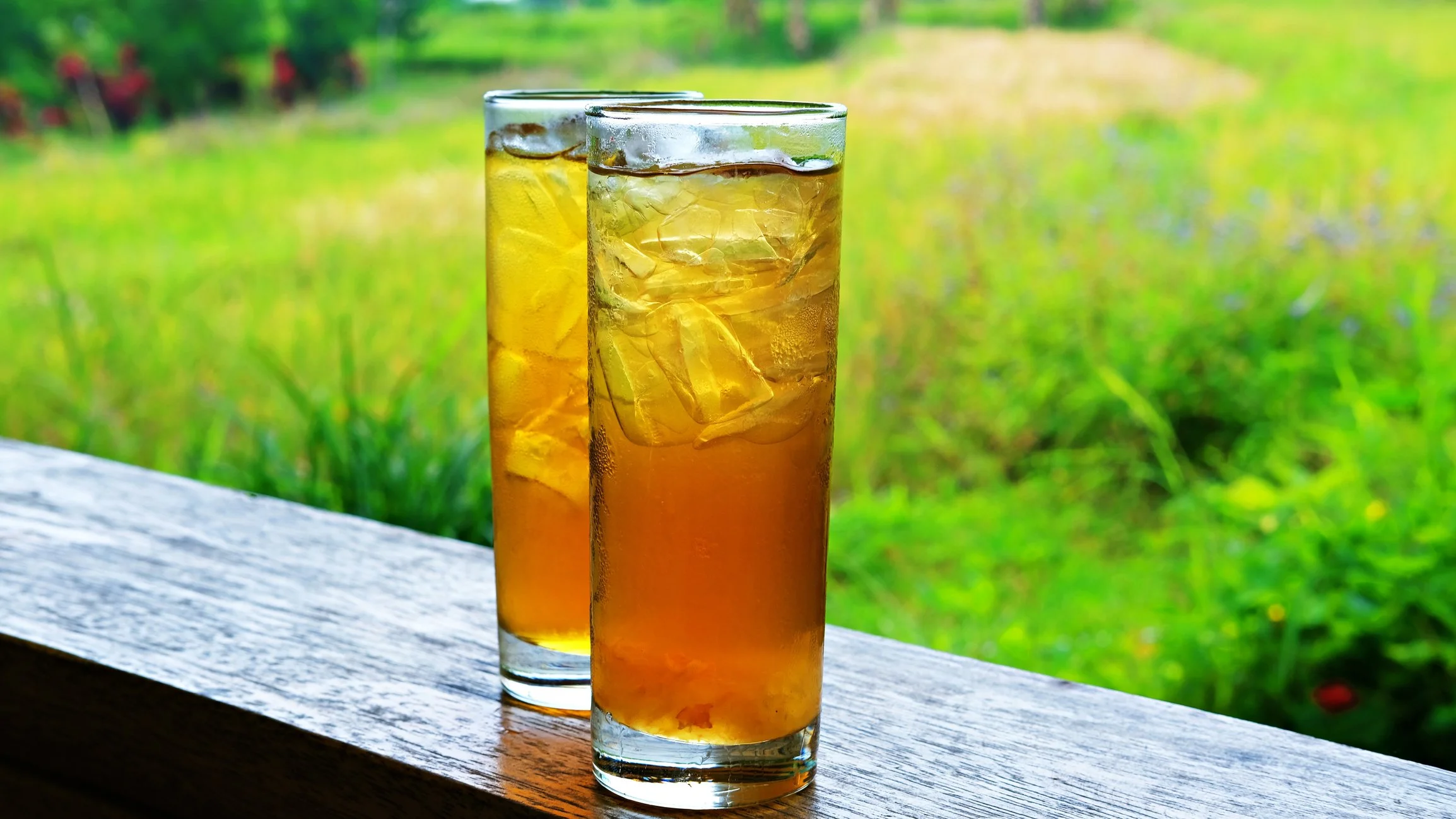 two glasses of black iced tea with a green lawn in the background