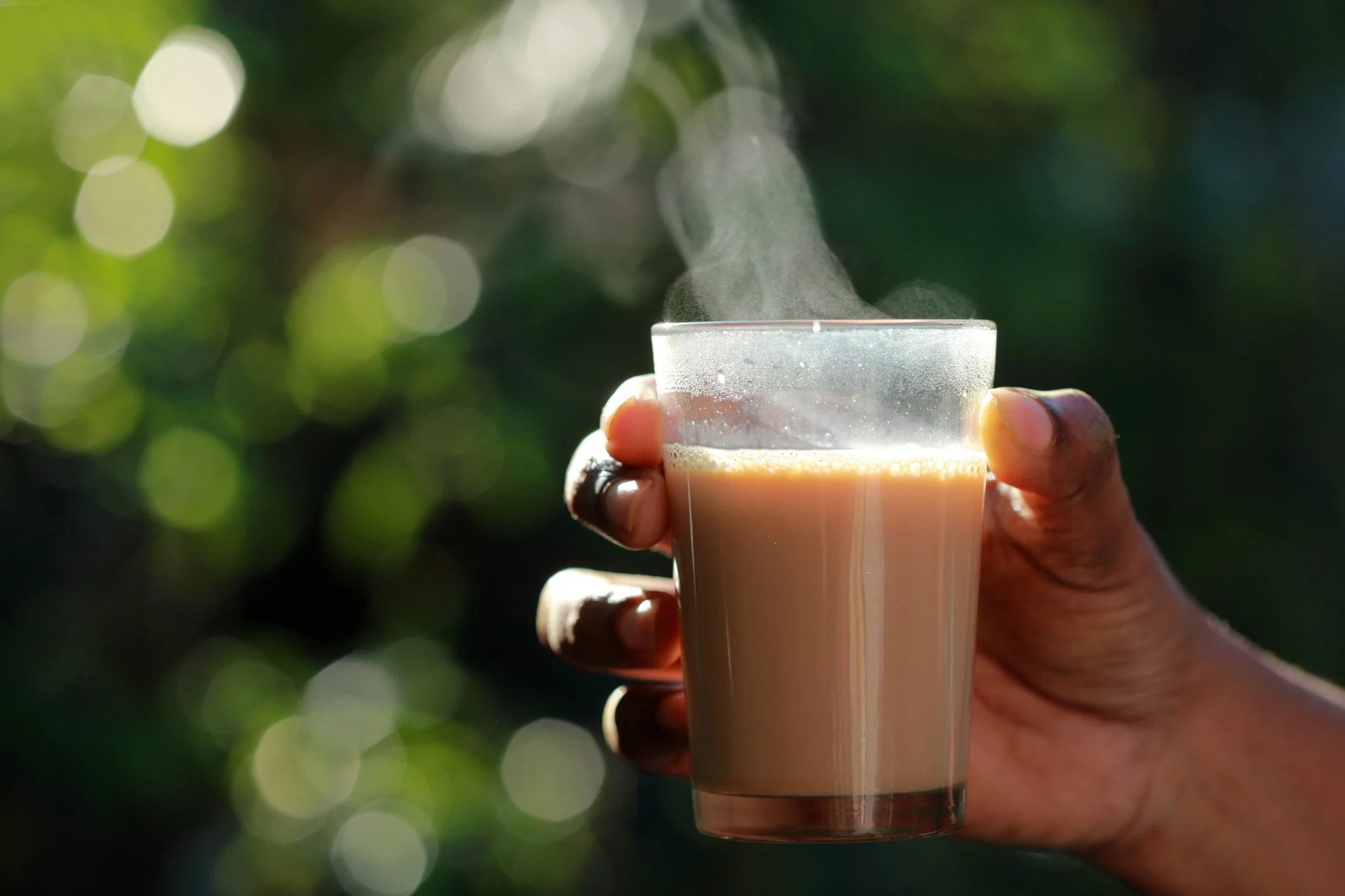 a hand holding a glass of hot chai with steam rising