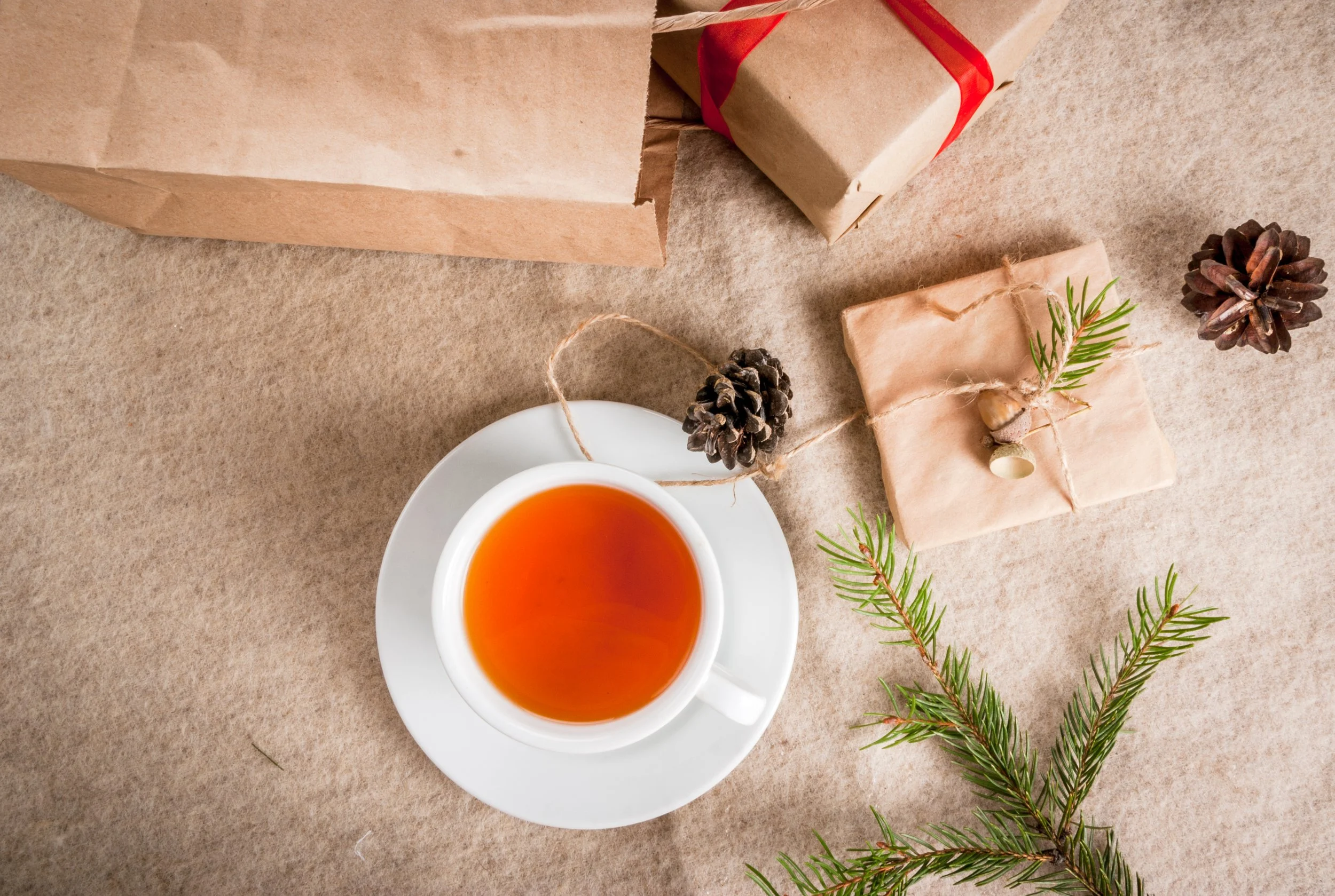 a cup of tea on a natural linen cloth surrounded by pine needles, pine cones, and packages wrapped in kraft paper