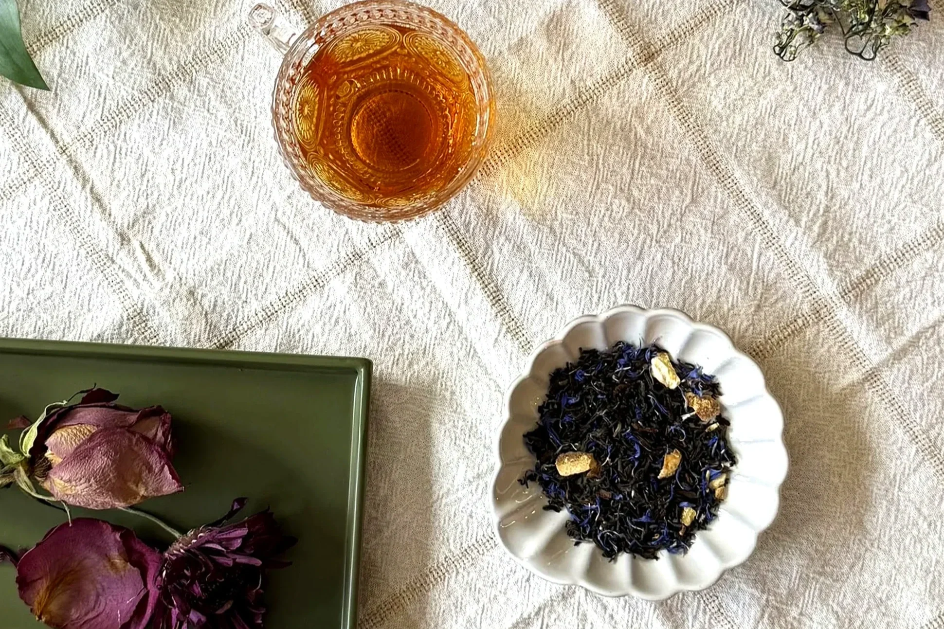 a cup of tea next to a dish of tea leaves and a tray with dried roses