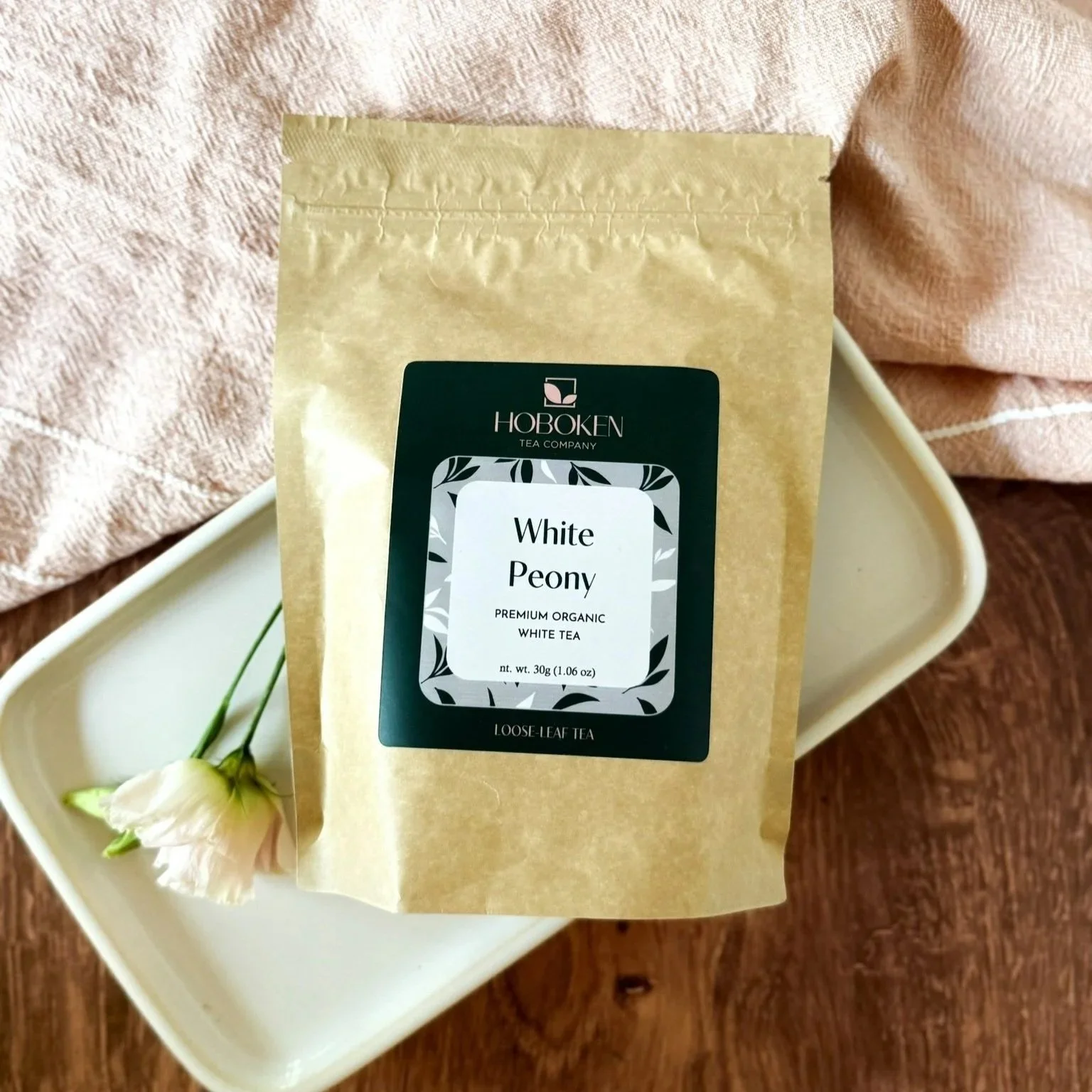a package of White Peony loose leaf organic white tea from Hoboken Tea Company next to a flower