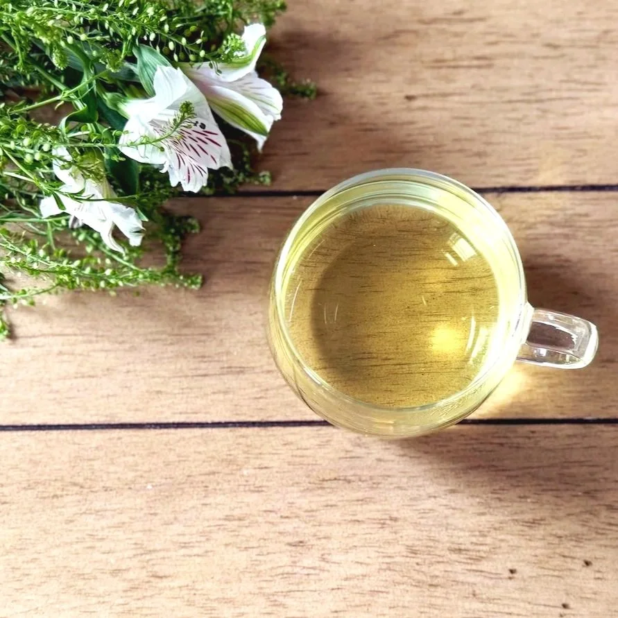 a glass cup of green tea on a table runner next to a bunch of white flowers