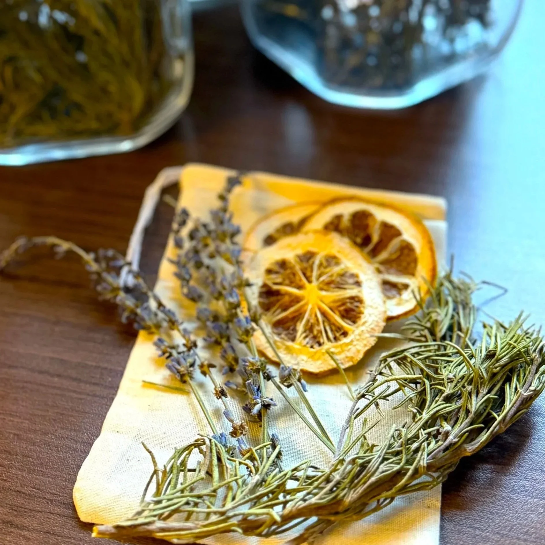 dried lemon slices, rosemary, and lavender on a small muslin bag on a table with jars of dried herbs in the background