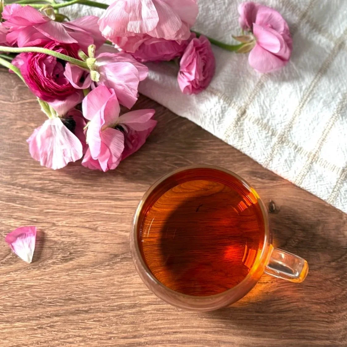 a glass cup of oolong tea on a wood table next to a bunch of pink flowers
