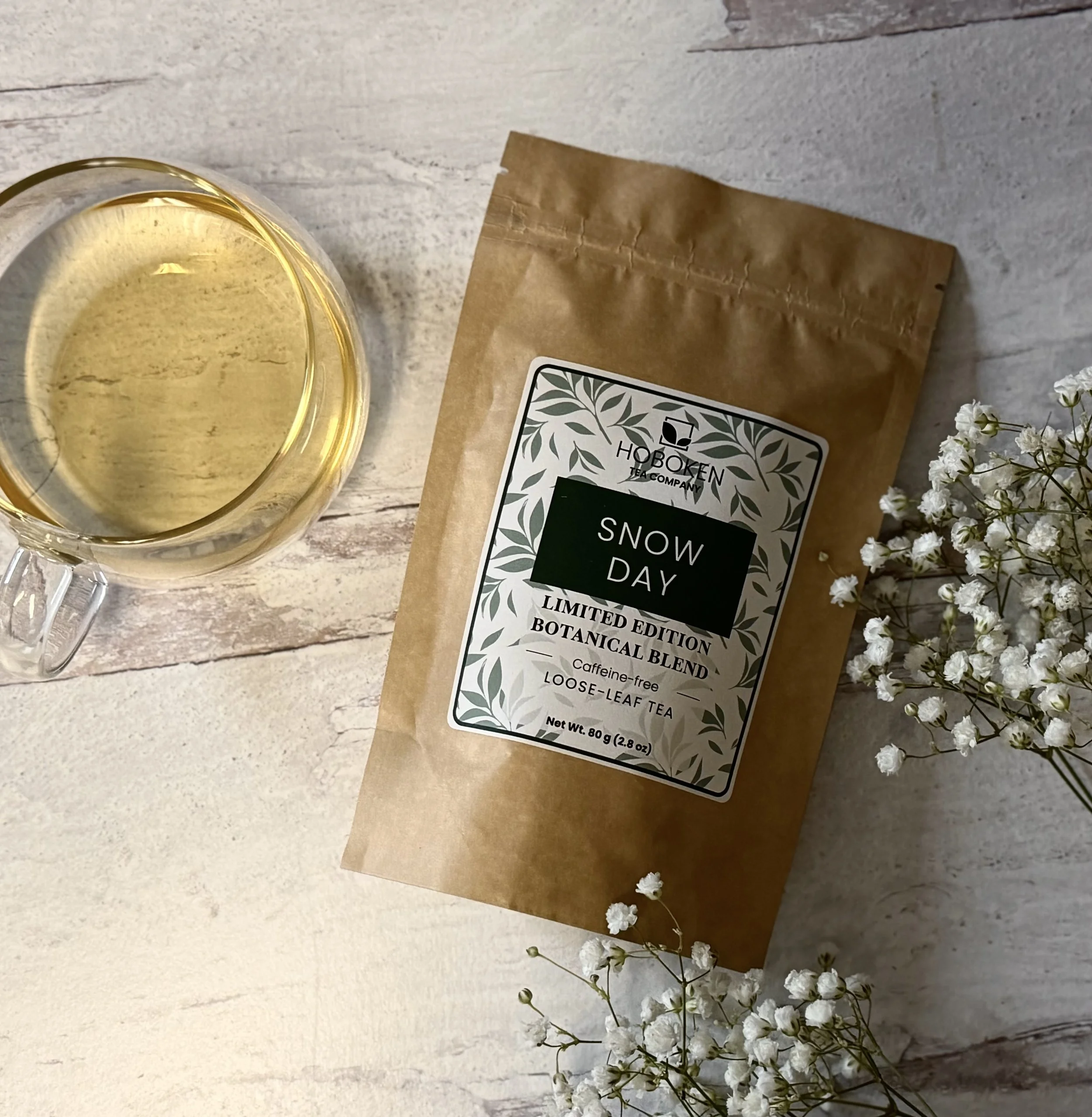 A package of Snow Day loose leaf herbal tea from Hoboken Tea Company on a light wood table next to a cup of herbal tea