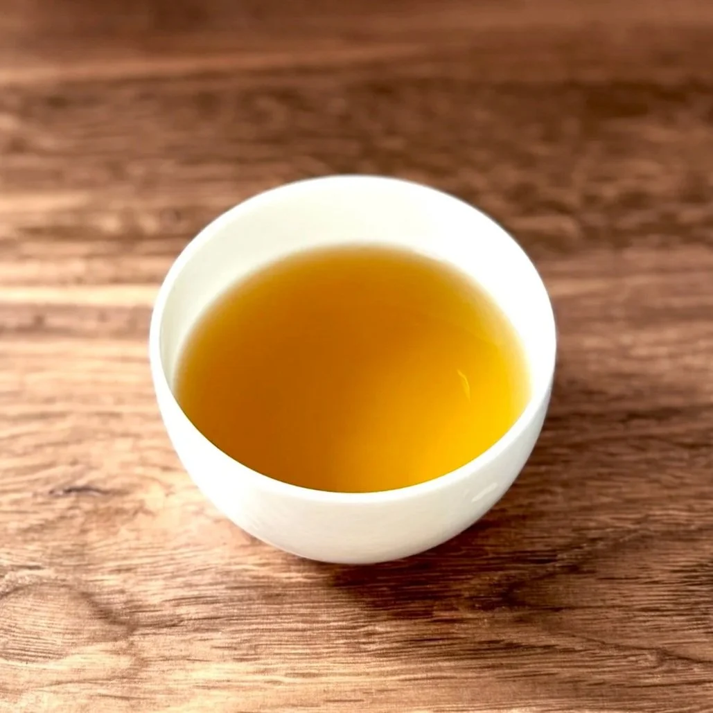 a white bowl of roasted green tea on a wood table