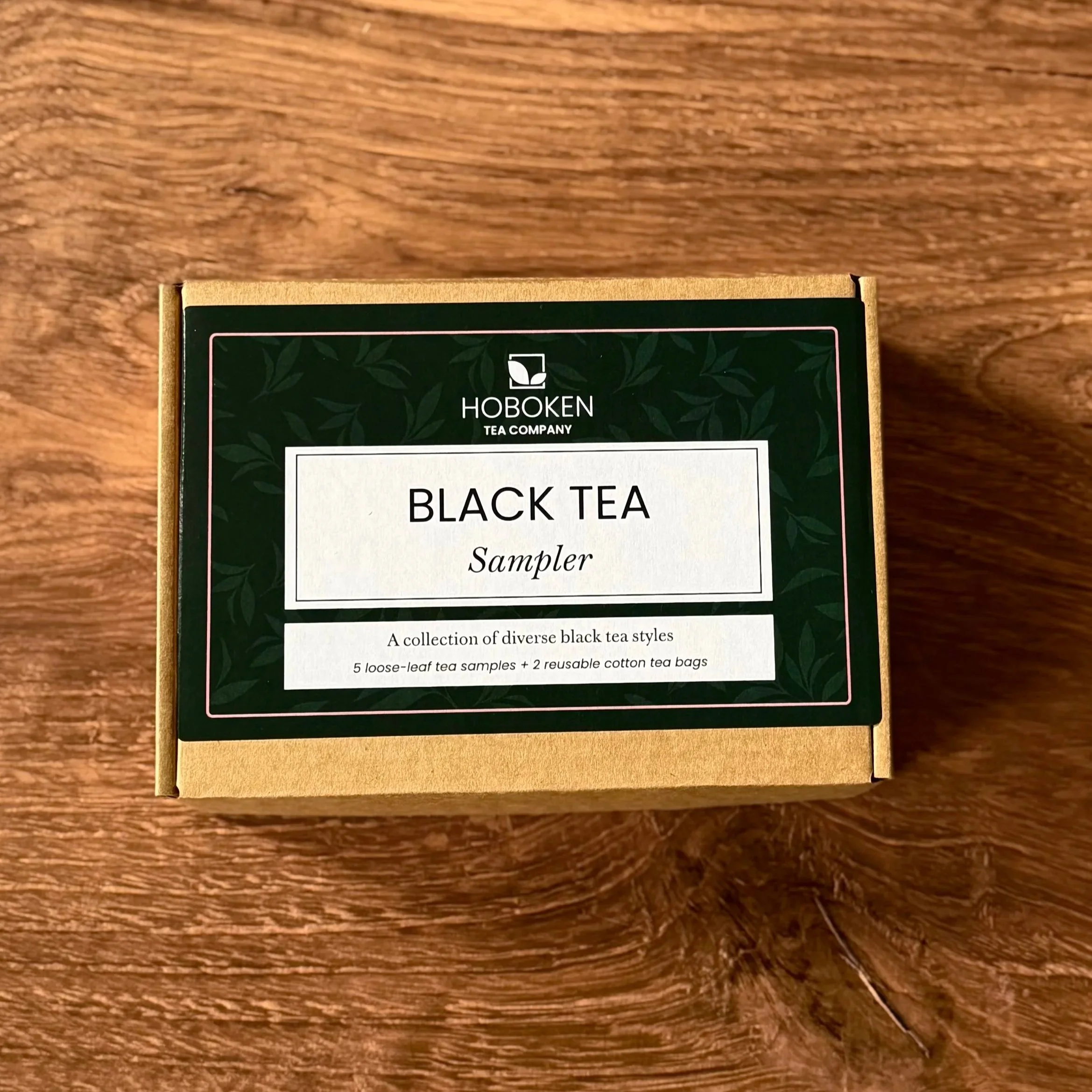 a small box with a green Hoboken Tea Company label reading "Black Tea Sampler" on a wood table