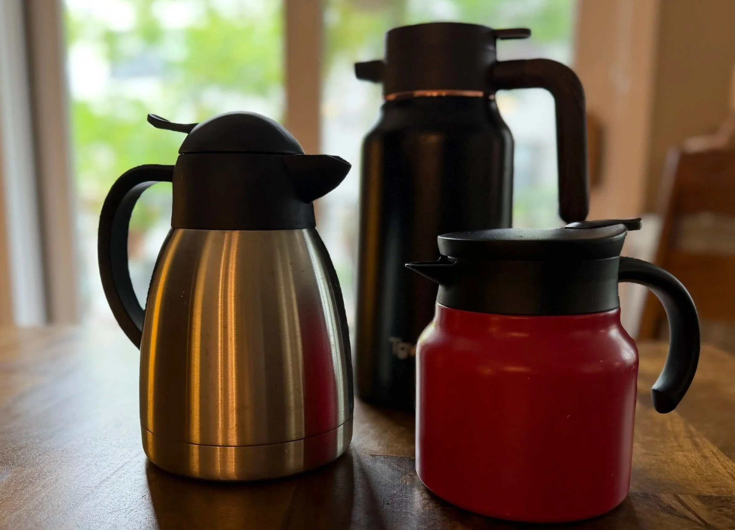 three insulated coffee carafes on a wood table
