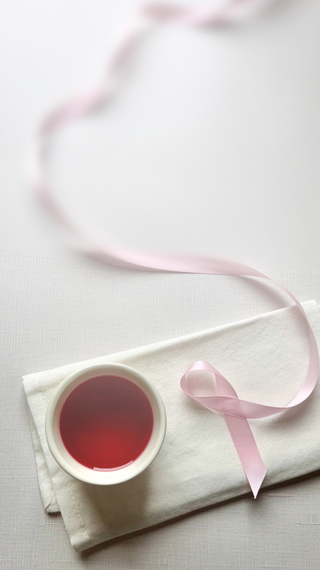 A cup of hibiscus herbal tea next to a pink ribbon for breast cancer awareness set on a cloth napkin