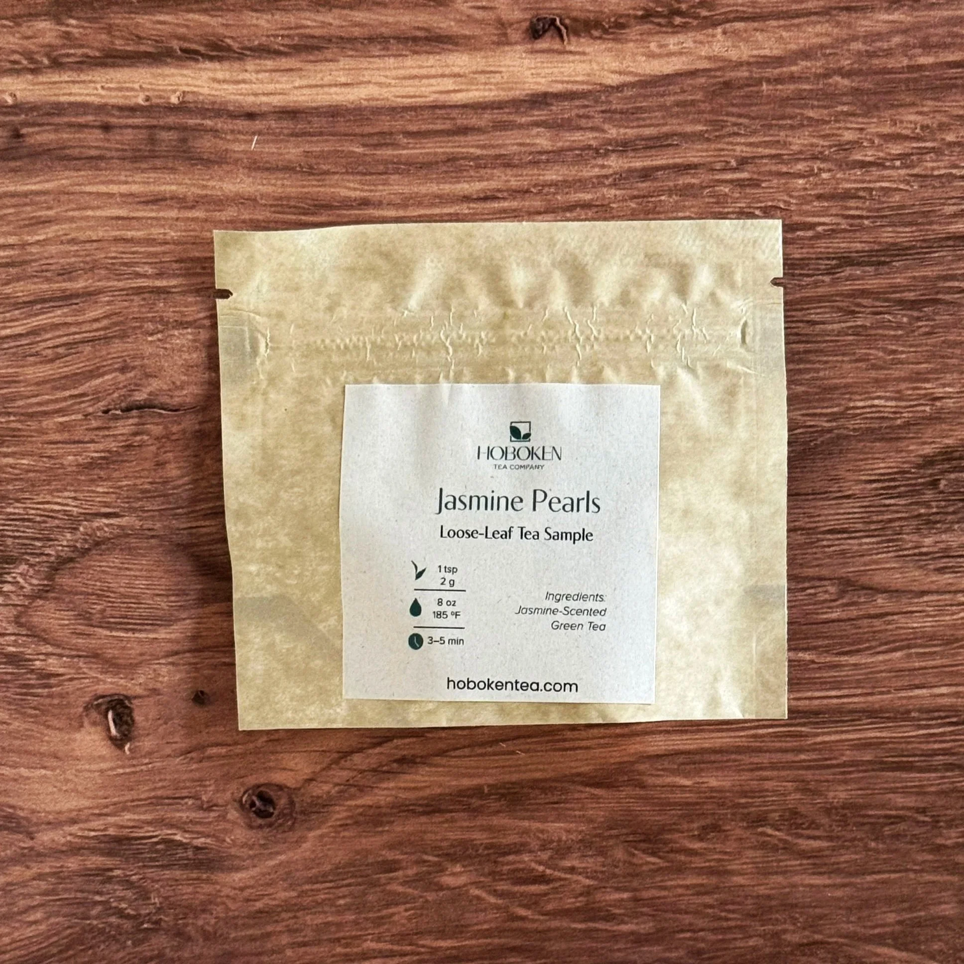 a sample size packet of loose leaf Jasmine Pearls green tea from Hoboken Tea Company on a wood table