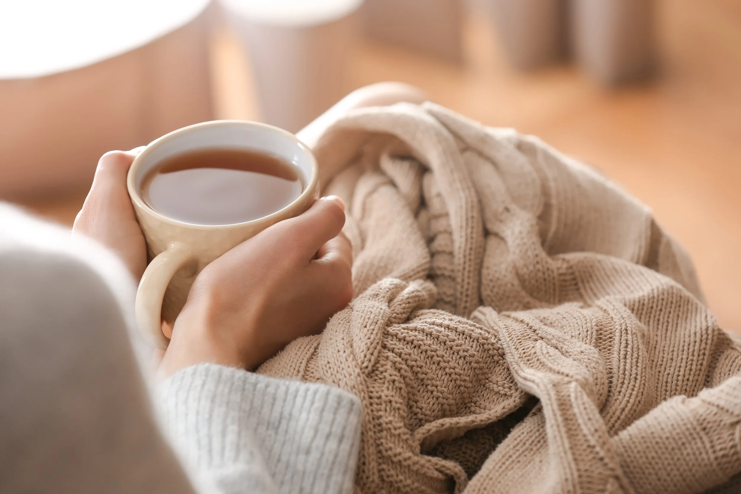 a woman sitting with a blanket on her lap and holding a mug of tea