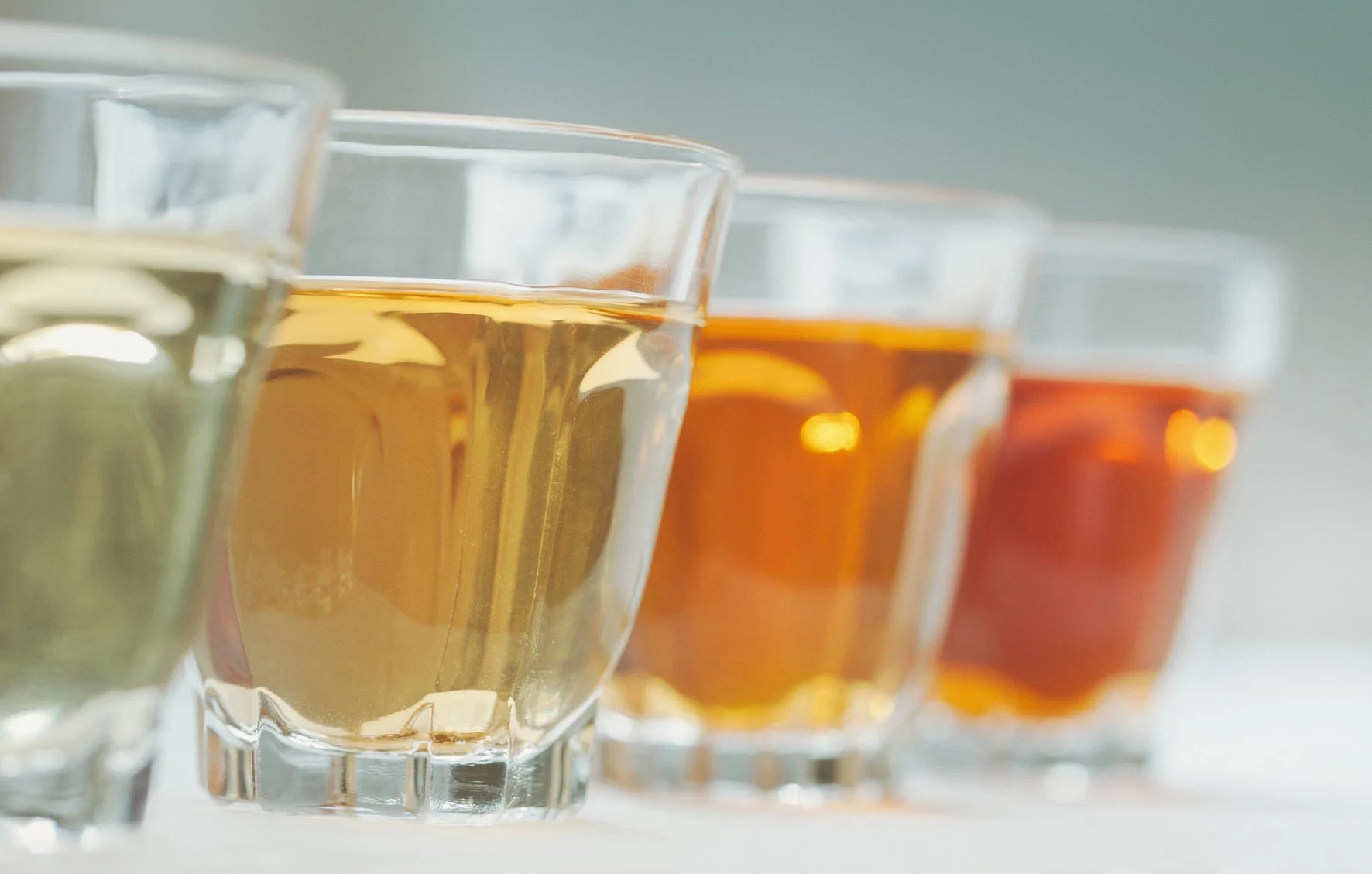 four glasses of tea of varying colors in a row