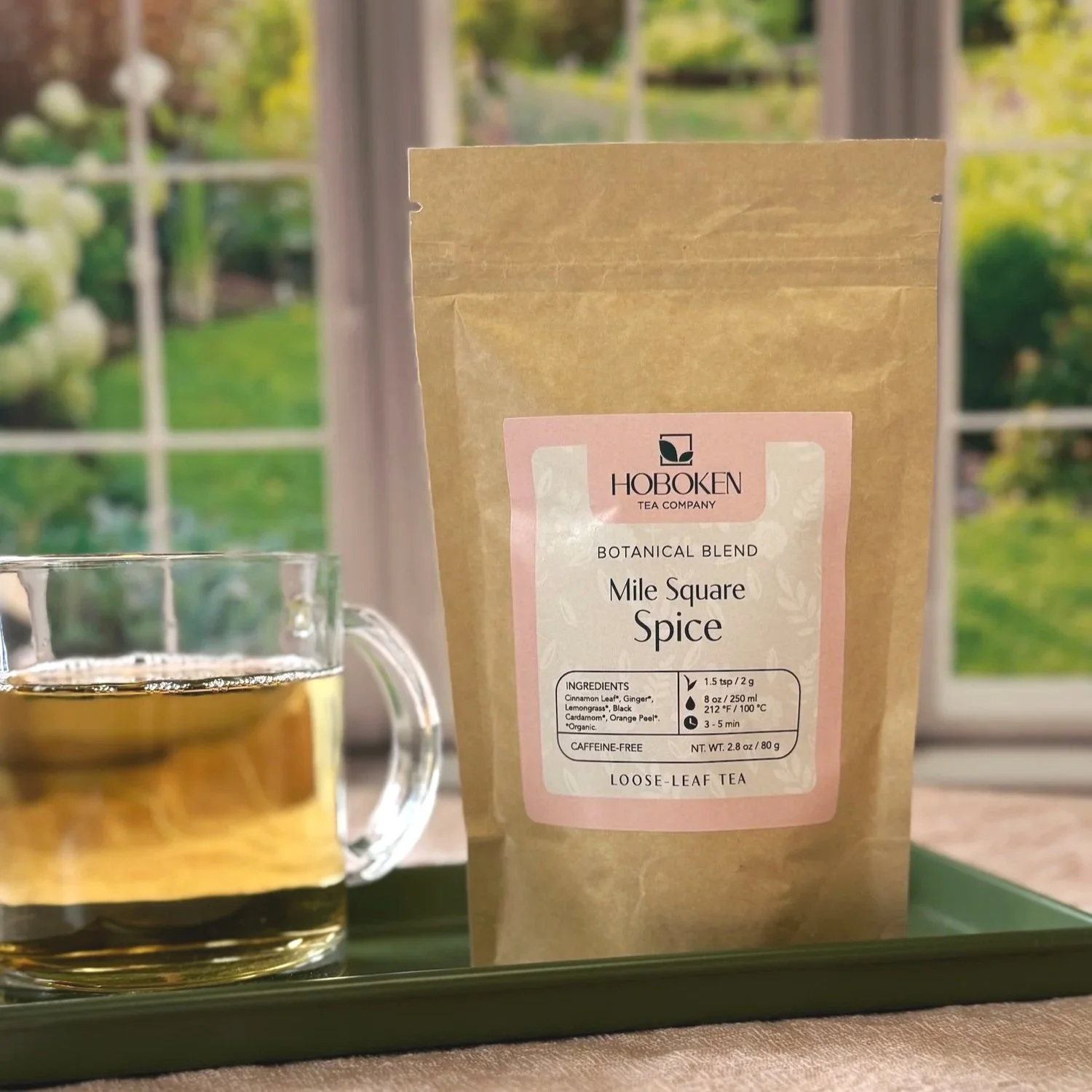a packet of Mile Square Spice caffeine-free herbal tea on a tray next to a cup of tea in front of a window with a sunny garden outside
