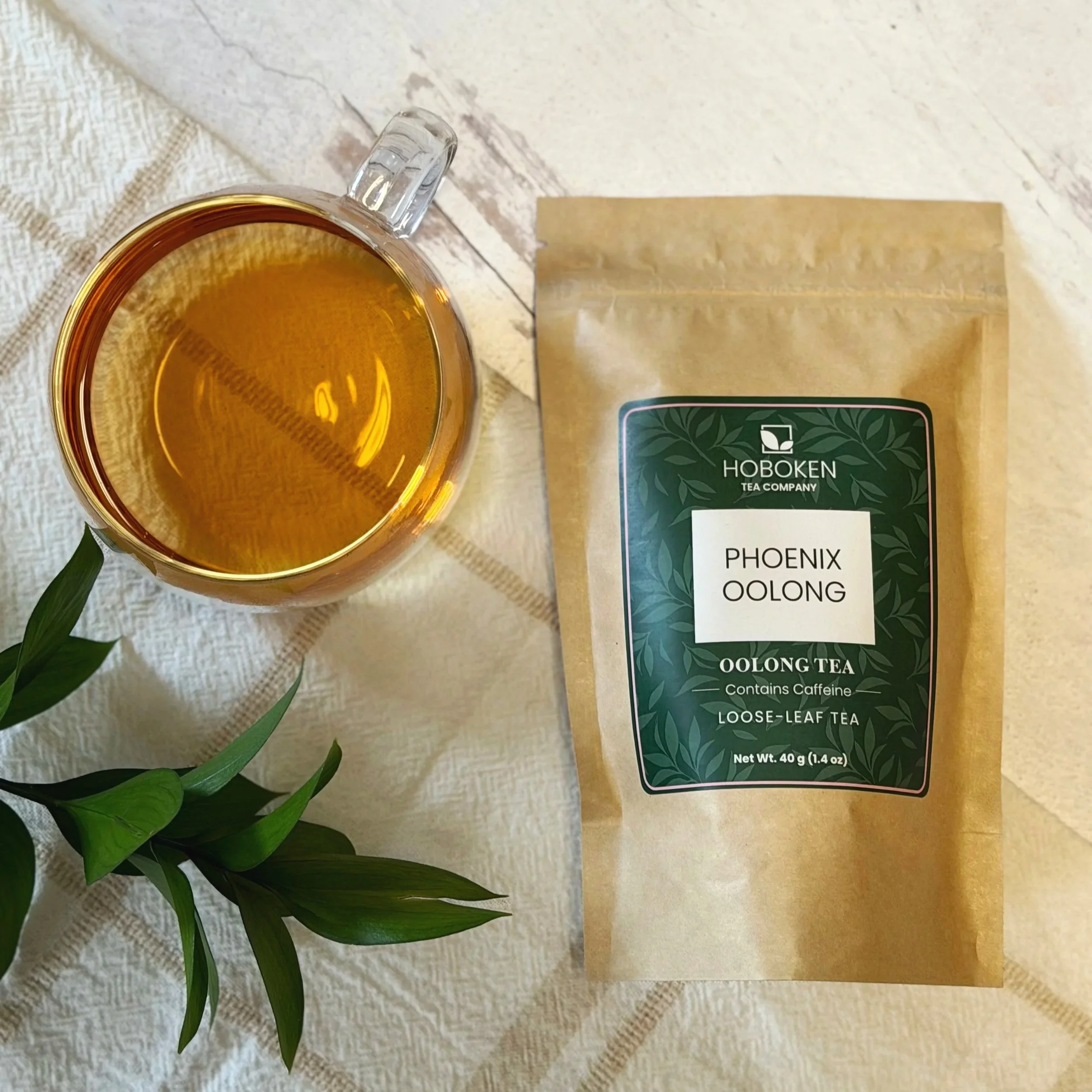 a package of loose leaf Phoenix Oolong tea from Hoboken Tea Company next to a glass of oolong tea on a light wood surface
