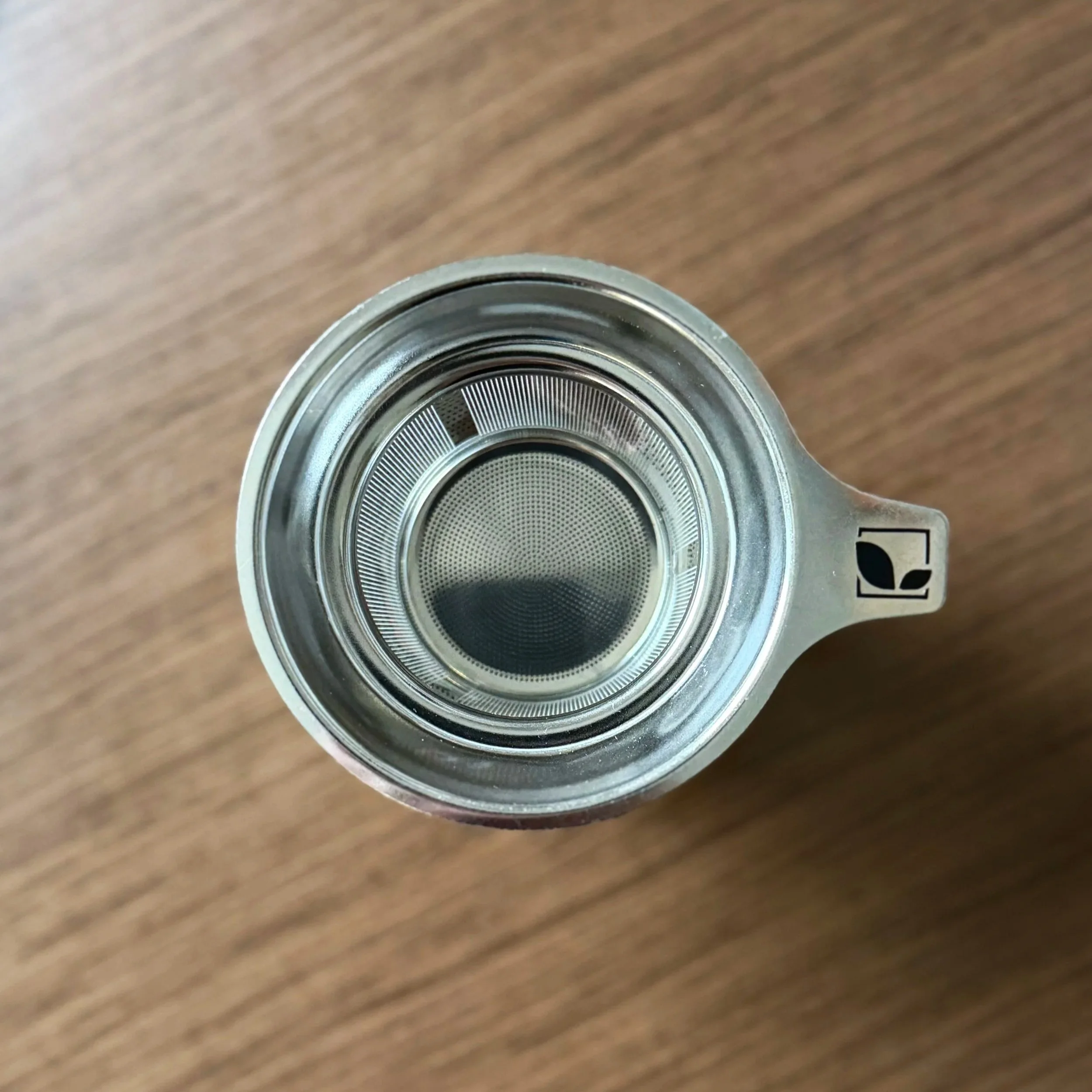 overhead view of a stainless steel tea infuser basket with a small Hoboken Tea Company logo on the handle