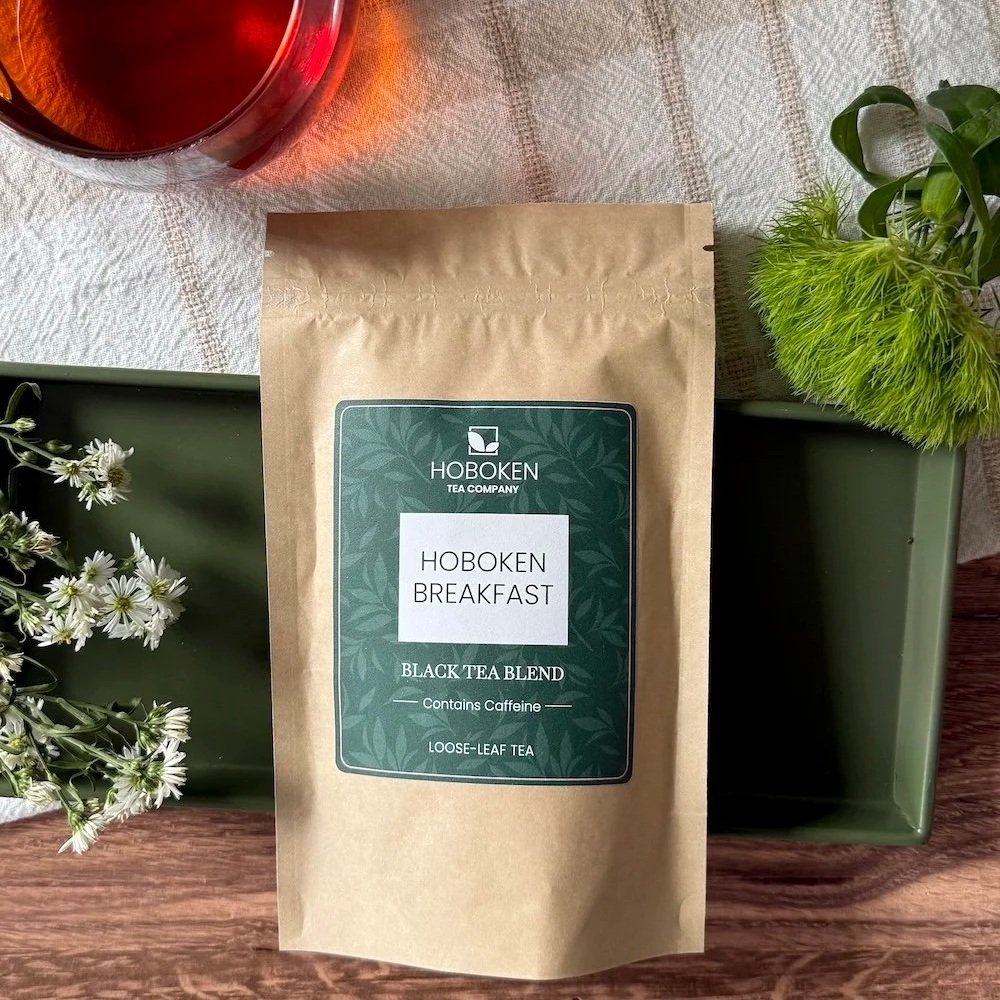 a package of Hoboken Breakfast loose leaf black tea on a green tray next to a cup of tea and some flowers