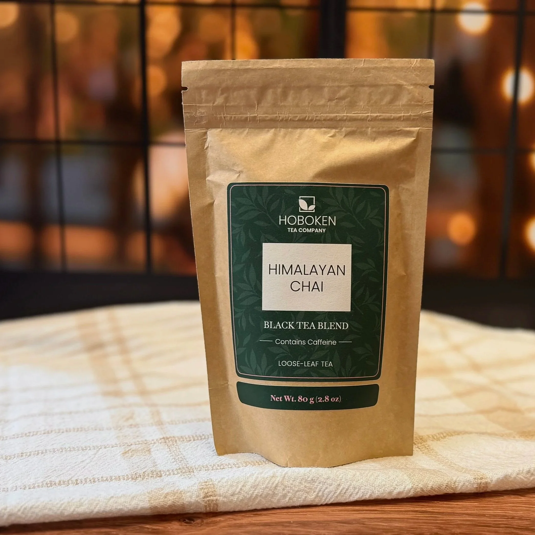 a package of loose leaf Himalayan Chai black tea from Hoboken Tea Company in front of a window with warm lights in the background