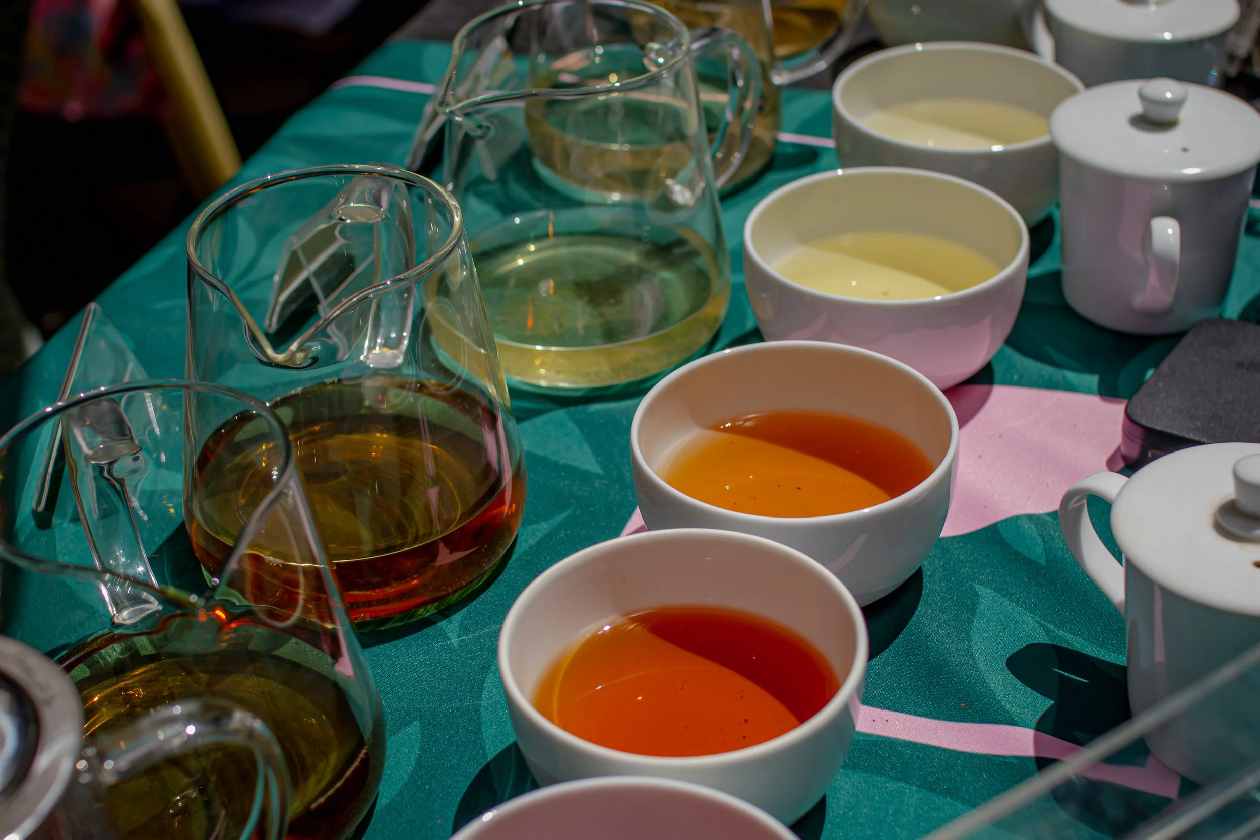 a row of teapots and white bowls full of tea on a green table runner