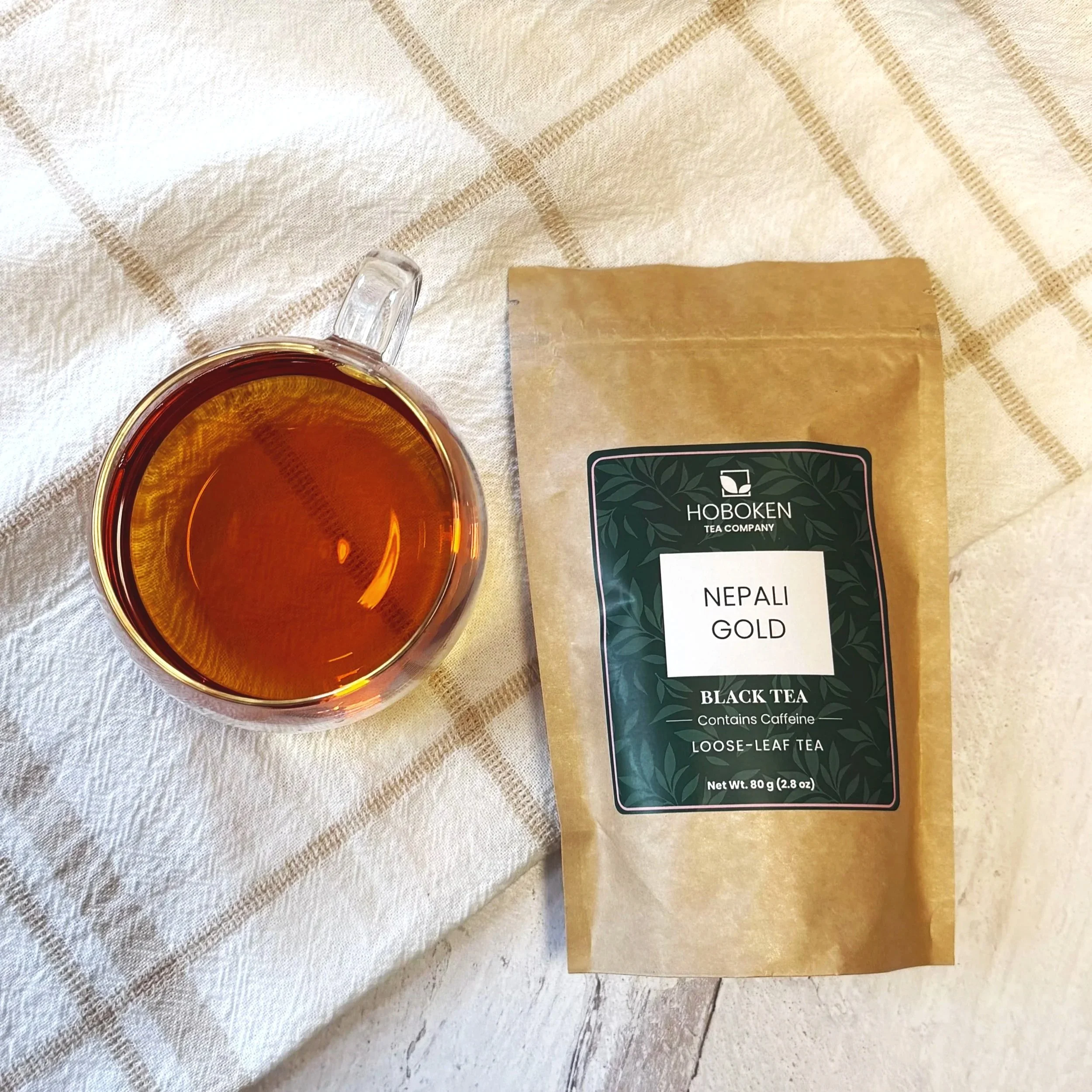 a package of loose leaf Nepali Gold black tea from Hoboken Tea Company next to a glass of black tea on a wood surface