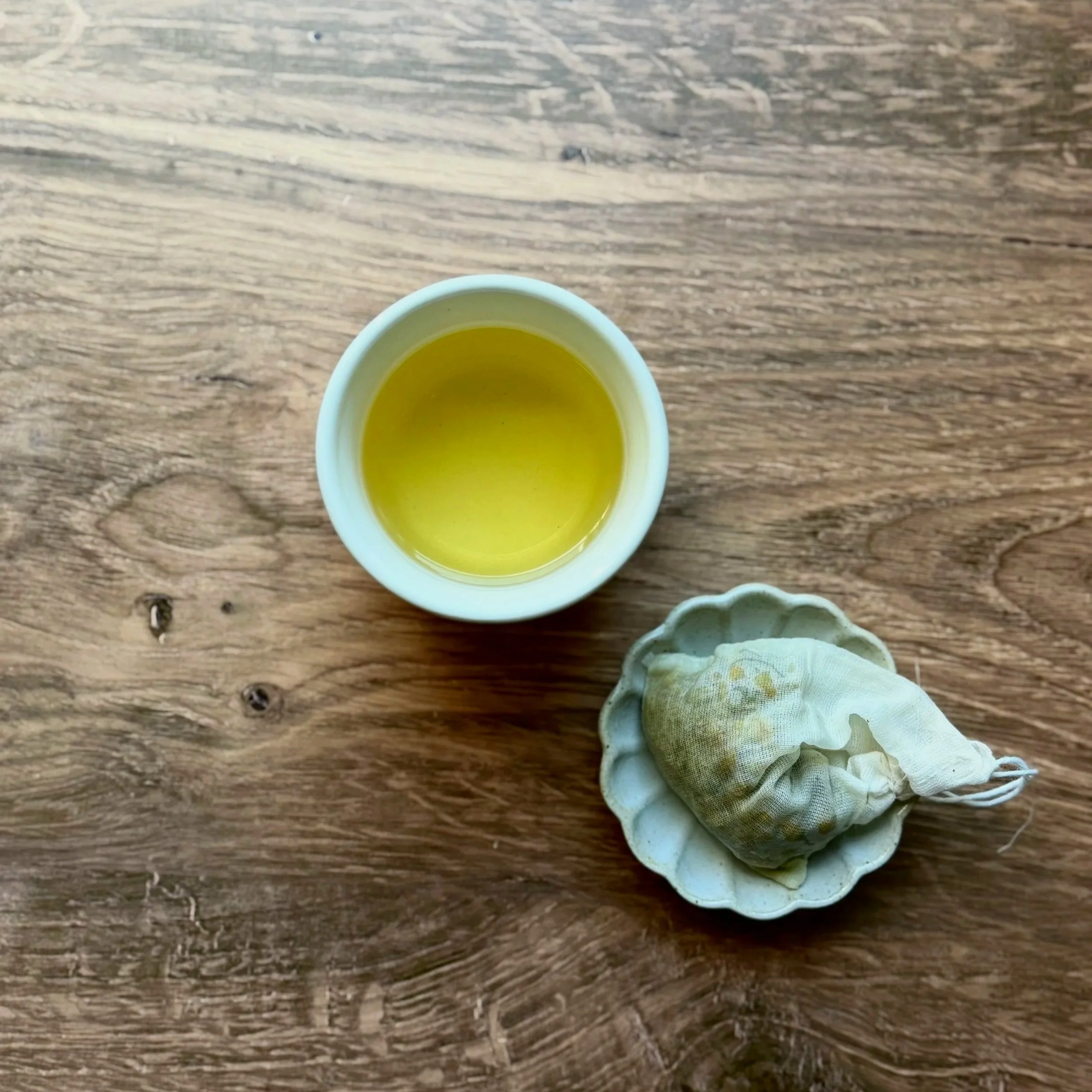 a cup of chamomile tea next to a small dish containing a used cotton tea bag