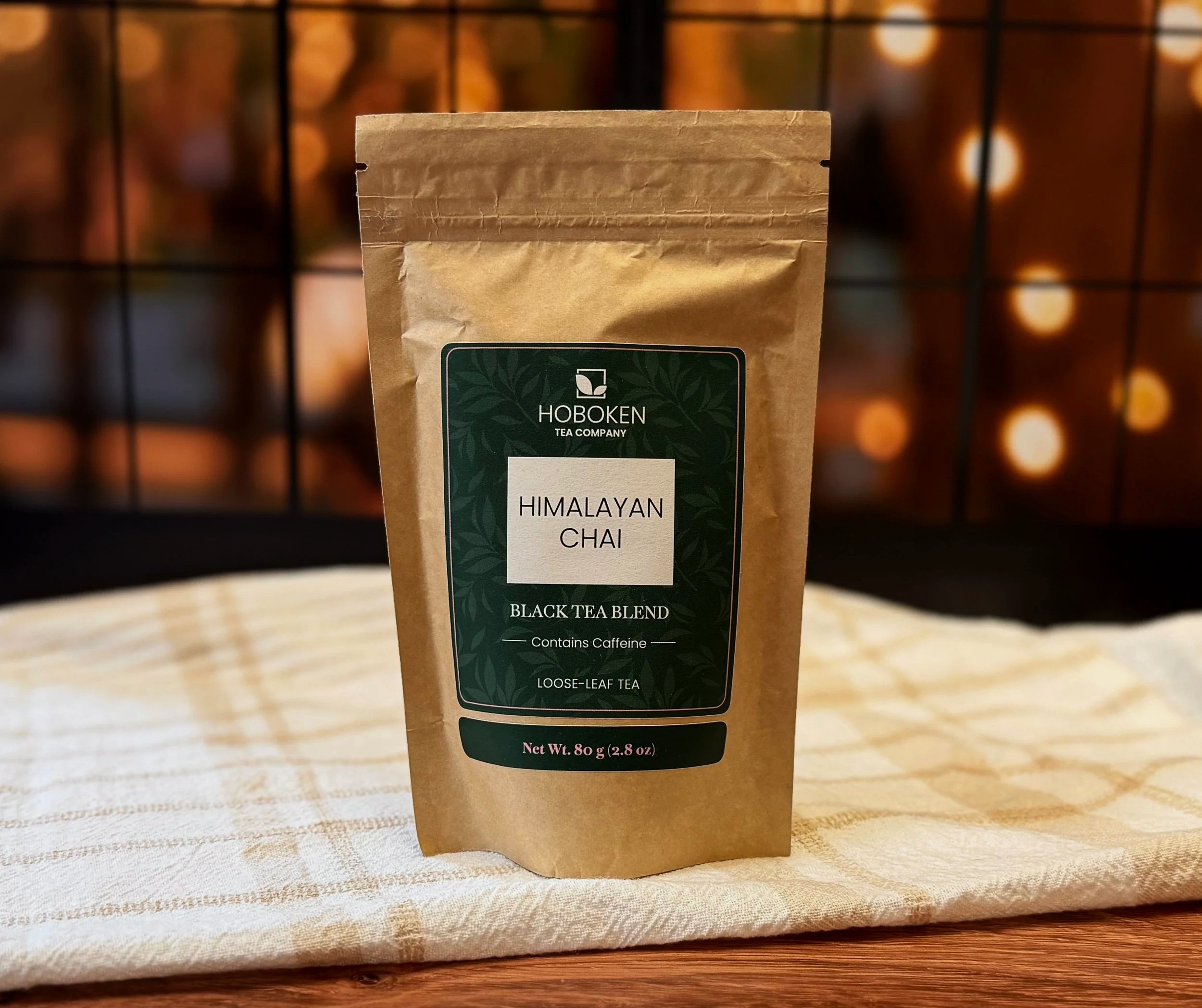 A package of Himalayan Chai loose leaf tea from Hoboken Tea Company on a wood table in front of a window with warm lights outside