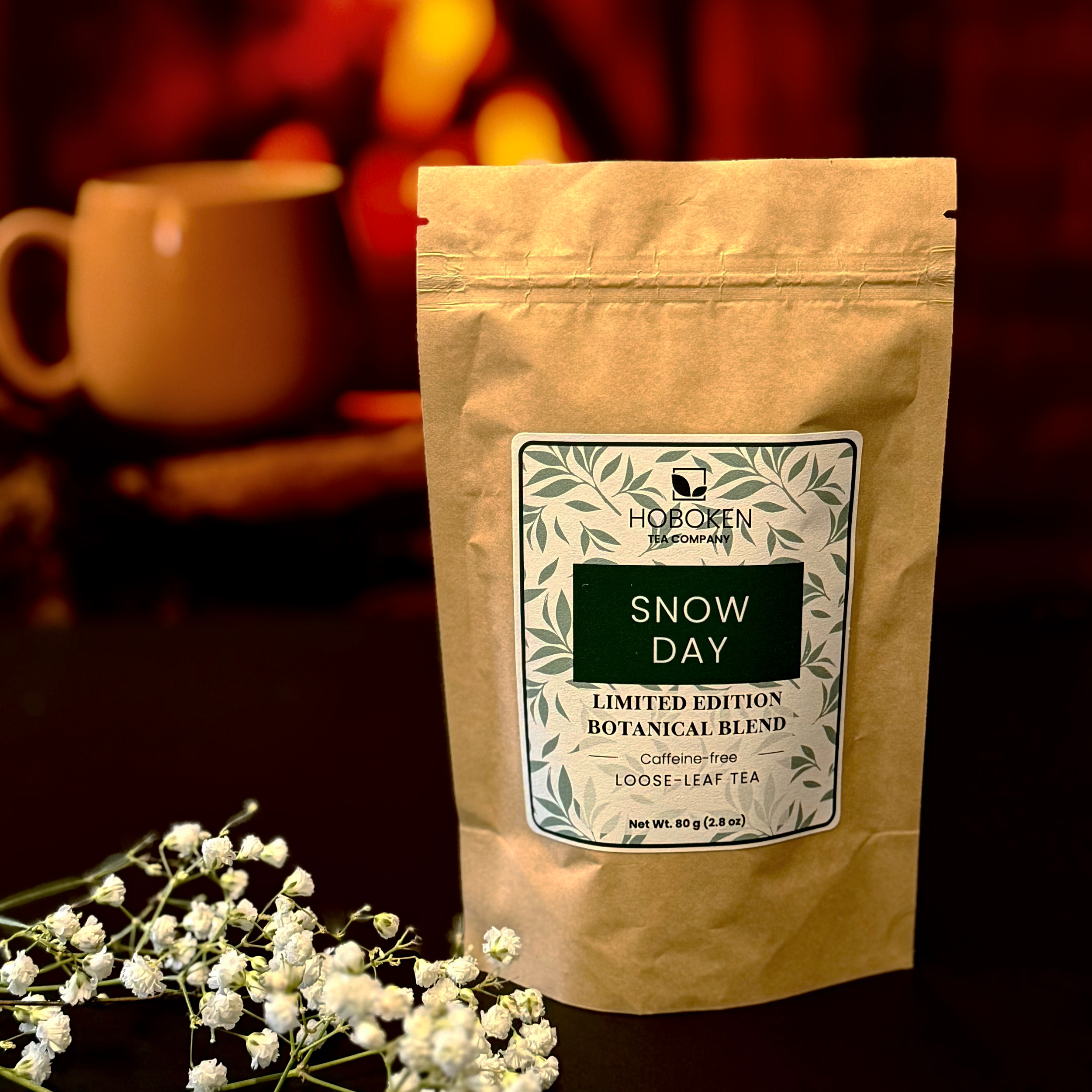 a package of Snow Day loose leaf herbal tea from Hoboken Tea Company in front of a fireplace and a coffee mug