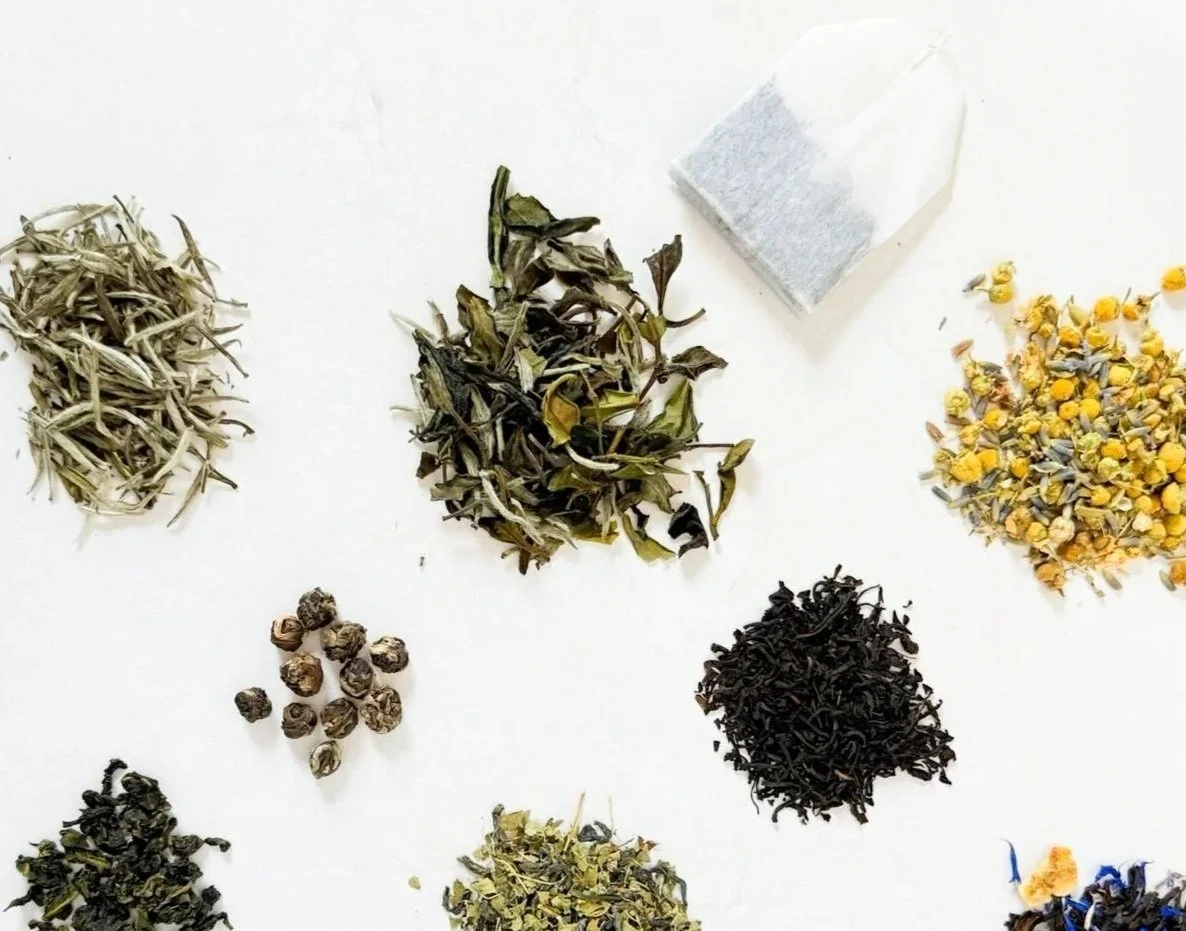 several piles of loose leaf tea and herbs next to a single tea bag
